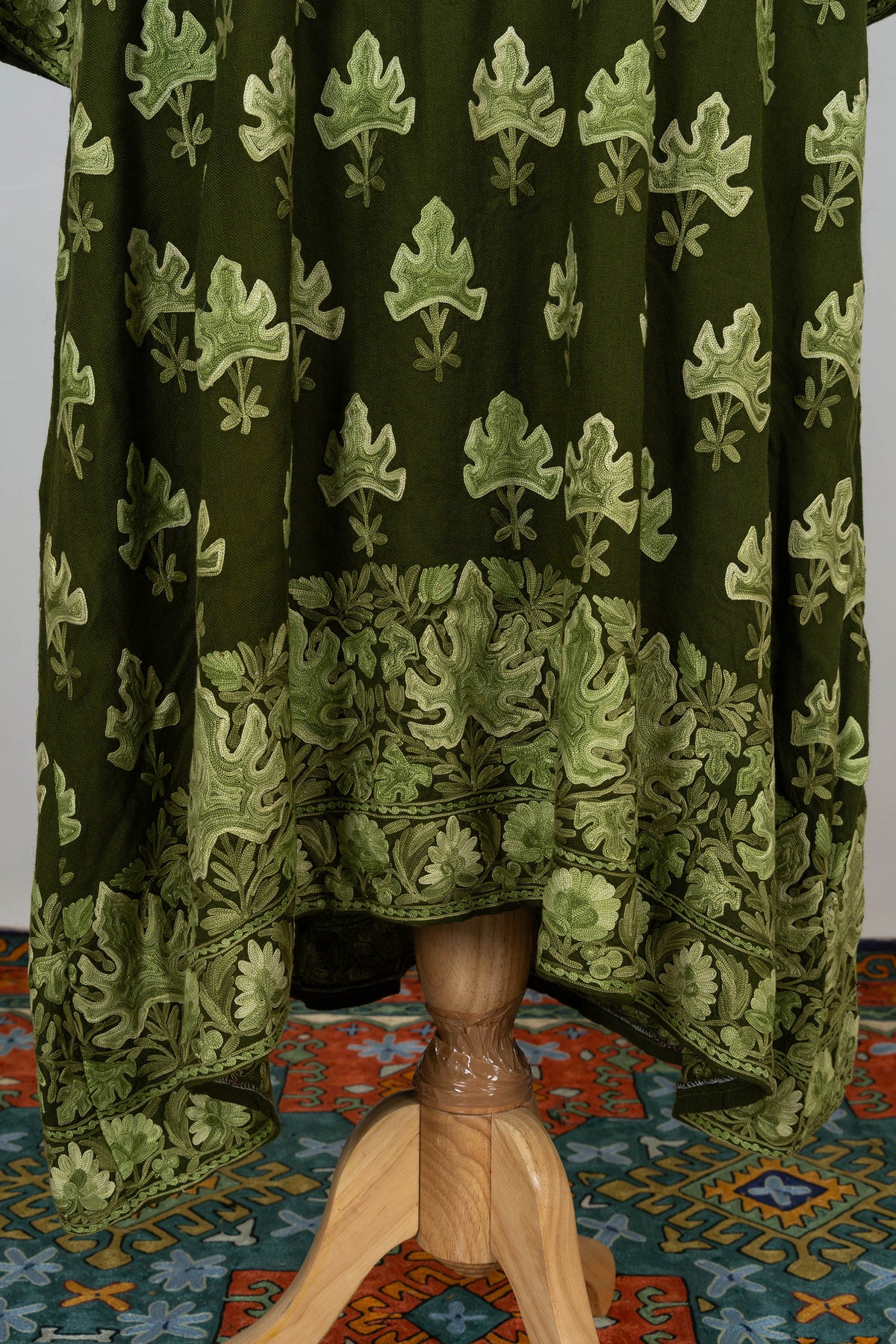 Lower abaya detail with scattered pale green leaves above a wide leafy and floral embroidered hem border.