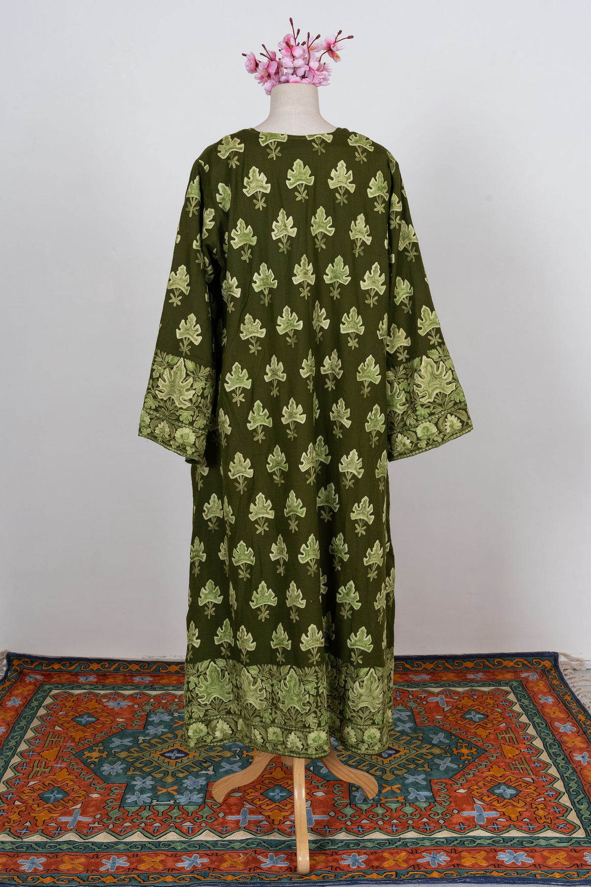 Full back view of the olive abaya with repeated leaf embroidery and broad floral-and-leaf borders at the cuffs and hem.