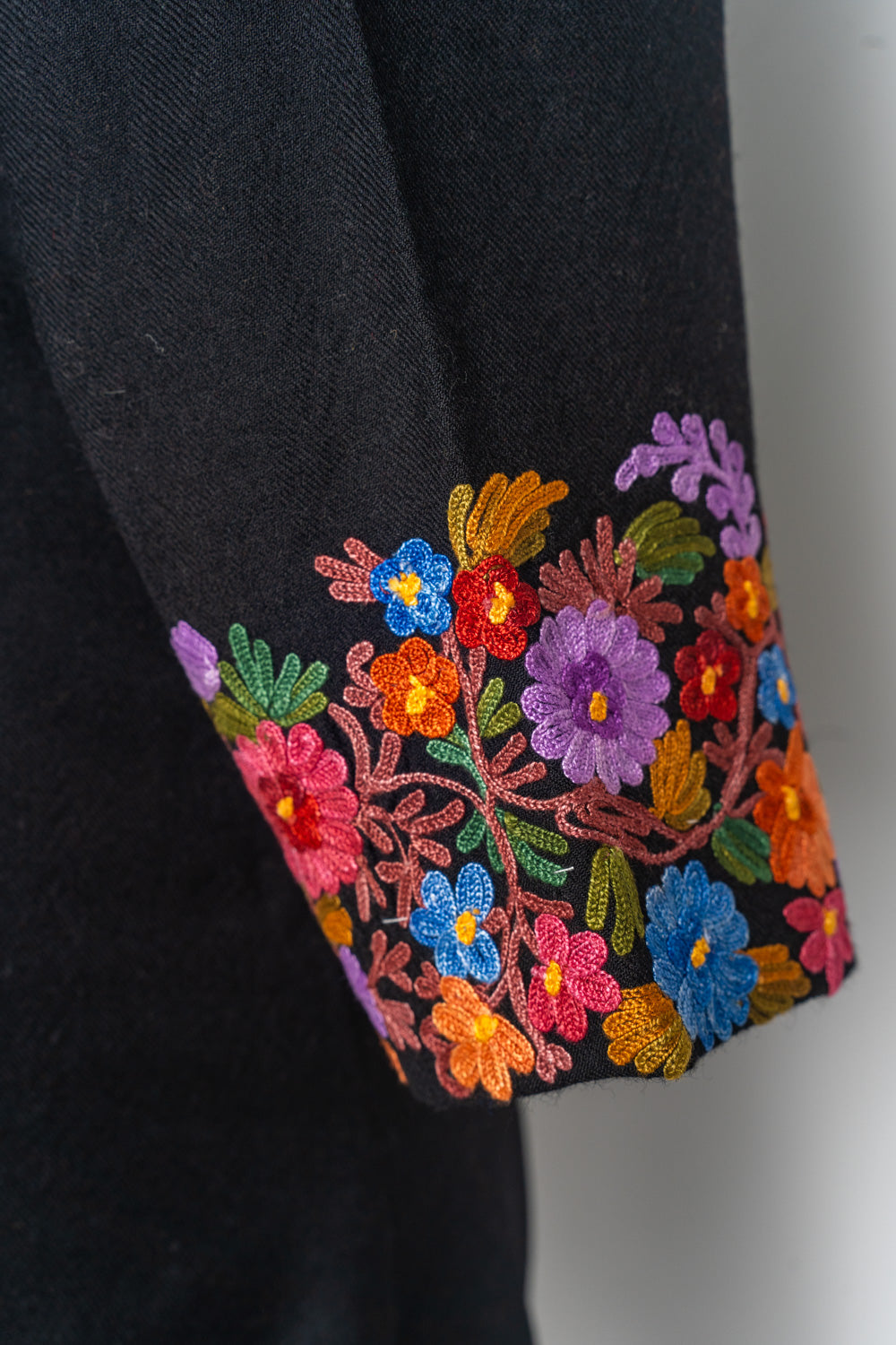 Black jacket cuff edged with bright blue, pink, purple and orange flowers and green leaves