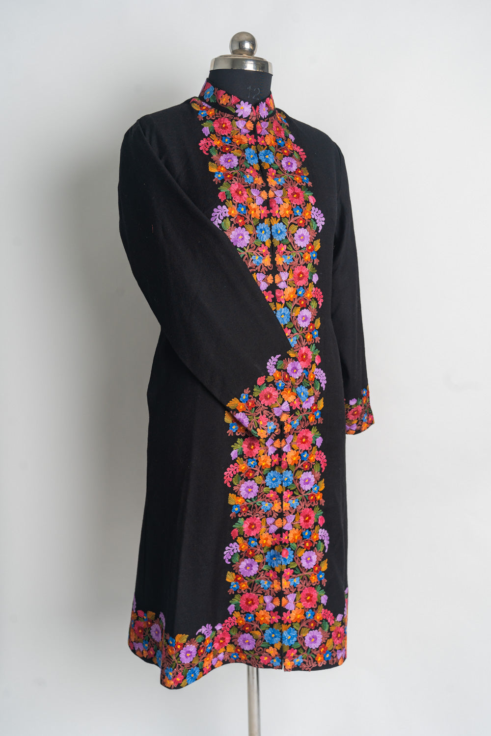 Angled full front of the black long jacket on a mannequin, with vivid floral borders and one sleeve crossed