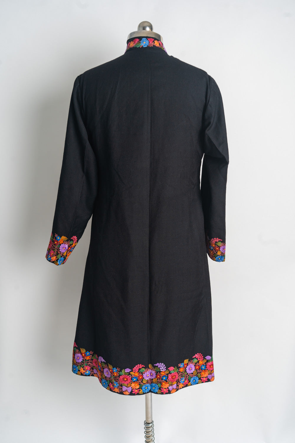 Back of the black long jacket with a plain centre and colourful floral embroidery around the collar, cuffs and hem