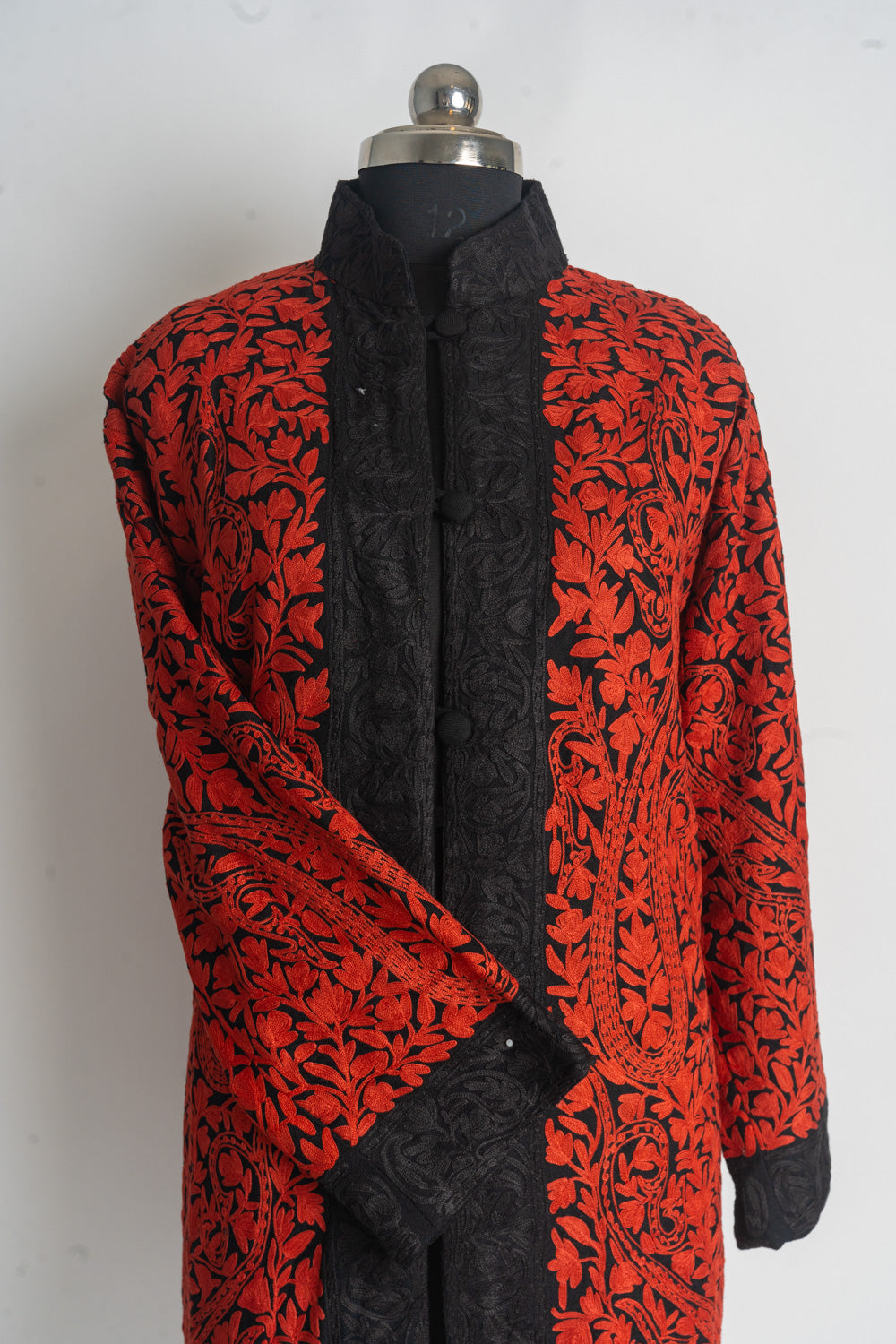 Upper front of a black jacket with bright red floral embroidery, black front borders and one sleeve across the body.
