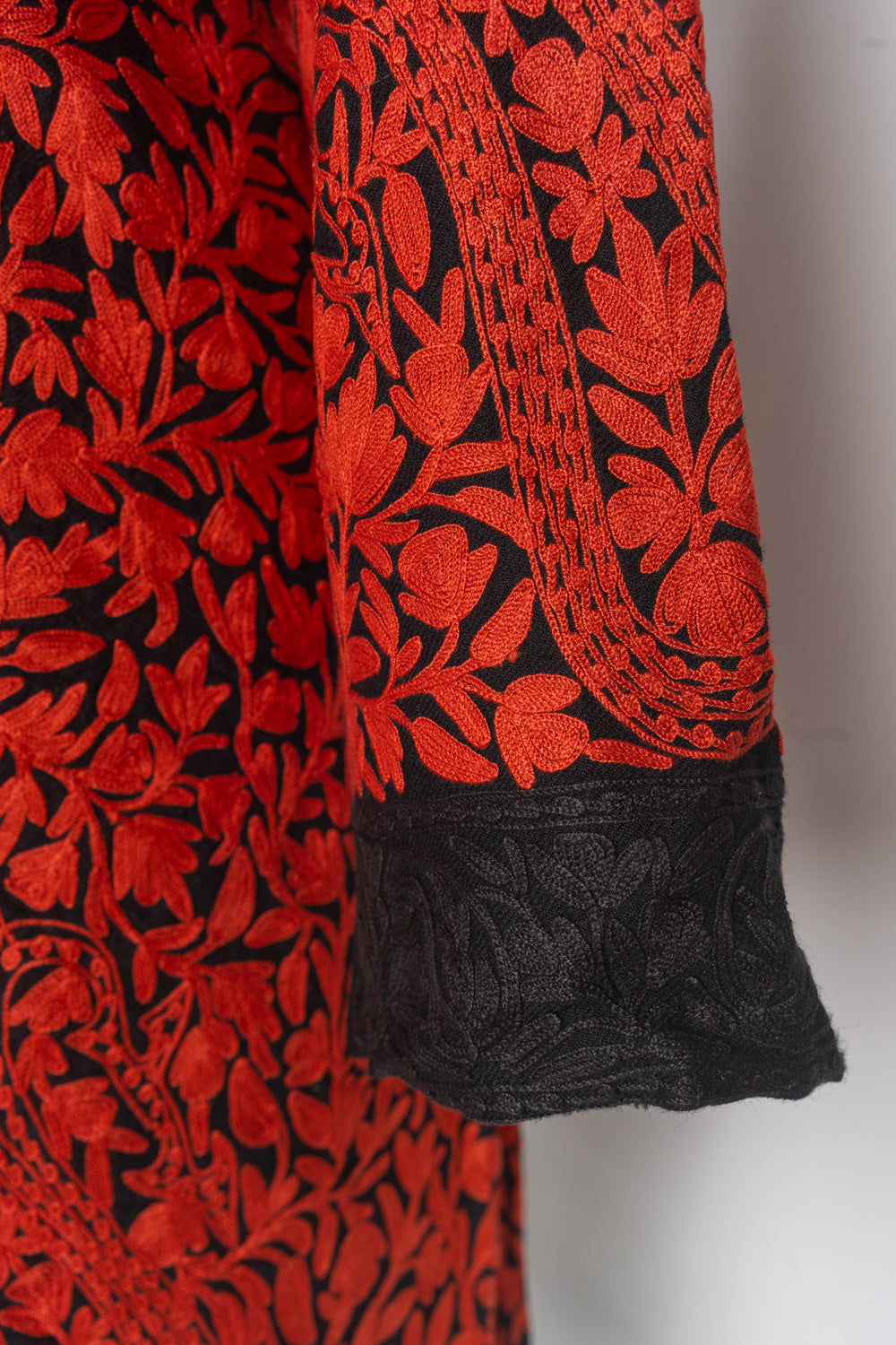 Sleeve detail of the red-and-black jacket showing red leafy embroidery above a broad tonal black cuff.