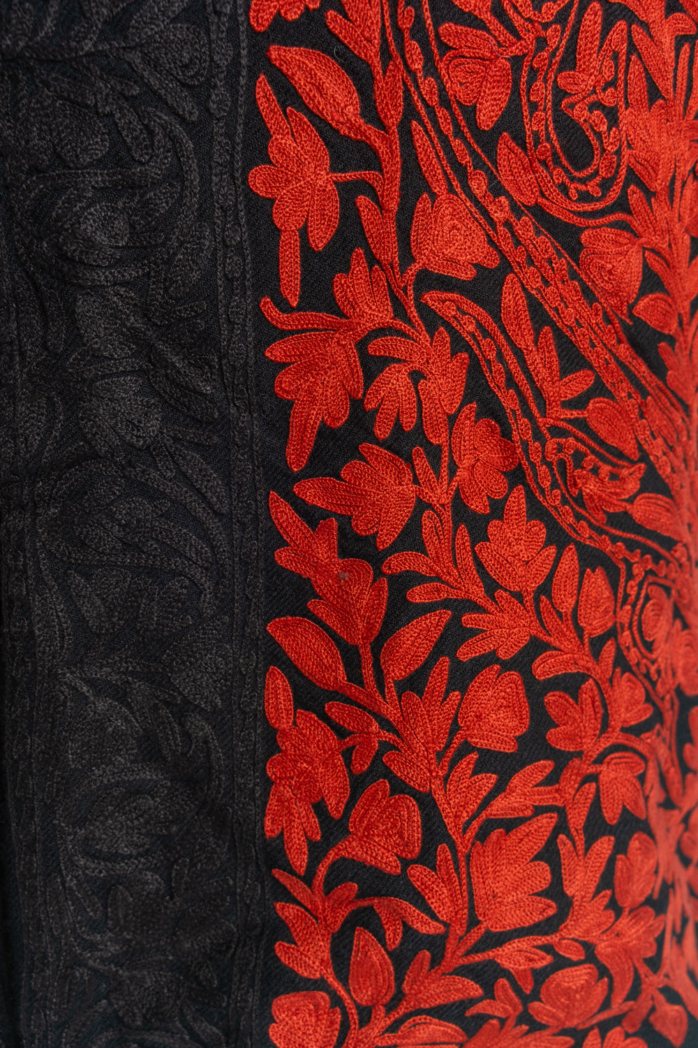 Close-up of bright red floral embroidery beside the jacket’s tonal black paisley front border.
