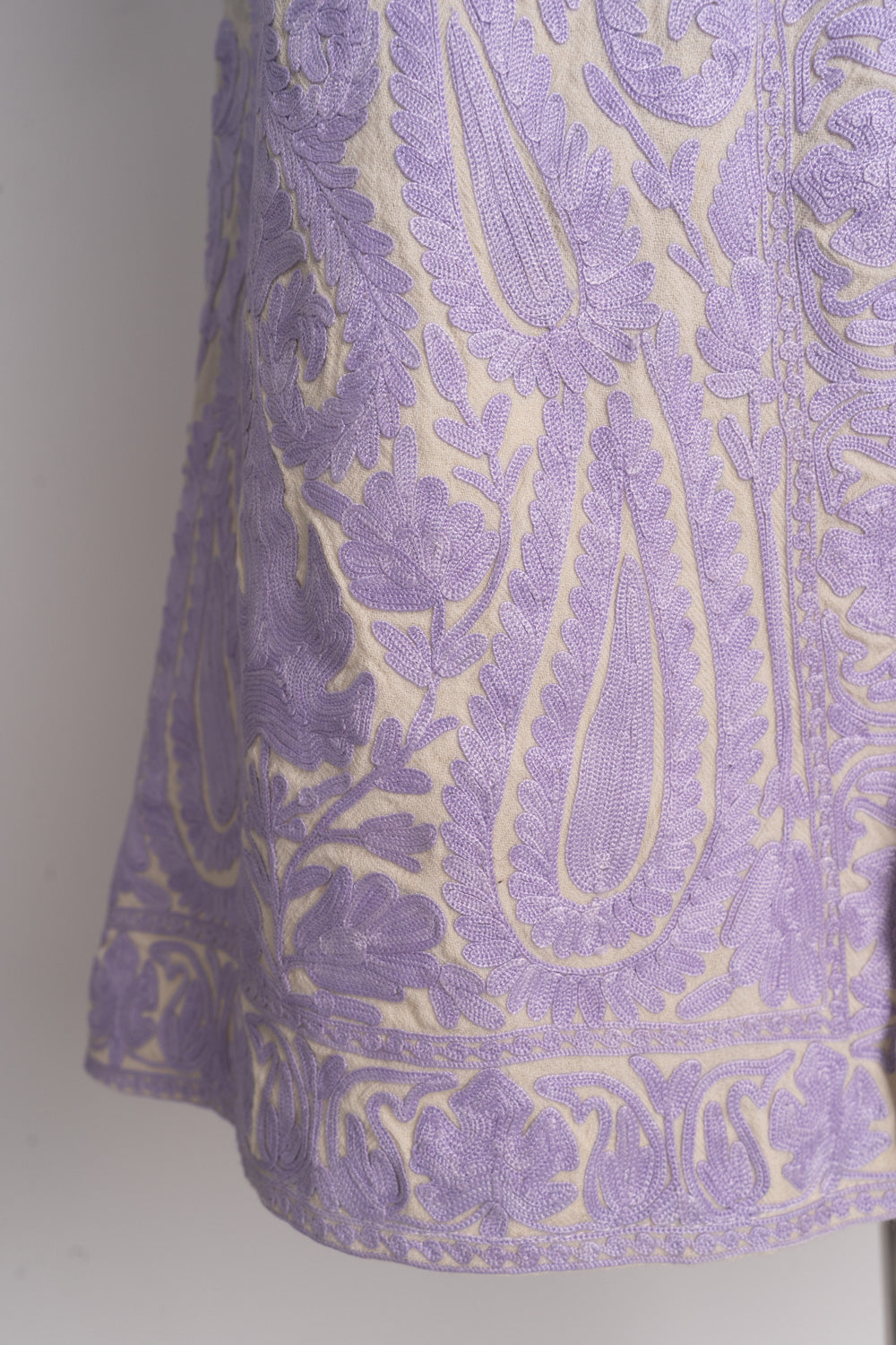 Lower corner of the cream jacket with large lilac paisleys, smaller flowers and a scrolling hem border
