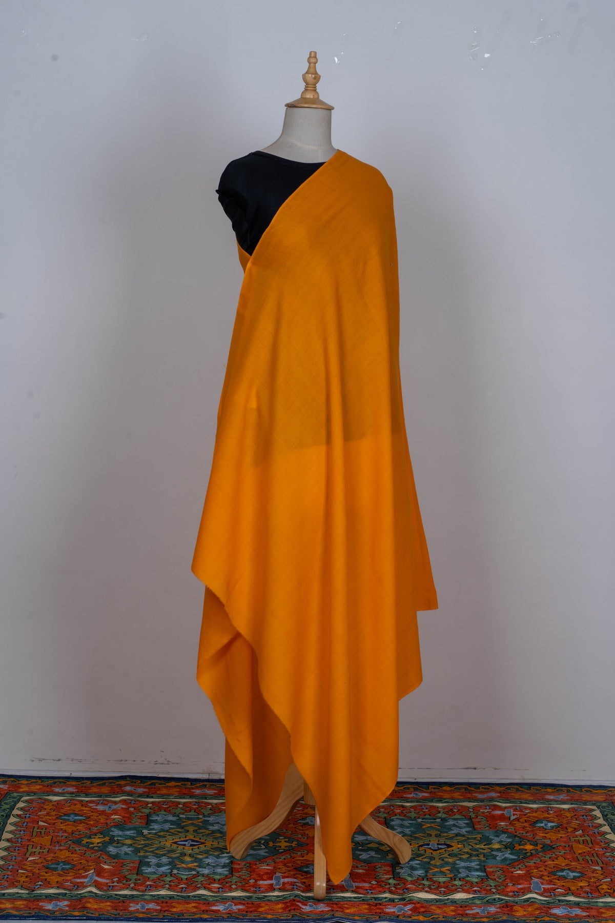 Full view of the golden-yellow wrap draped on a mannequin, with long folds and overlapping pointed ends.