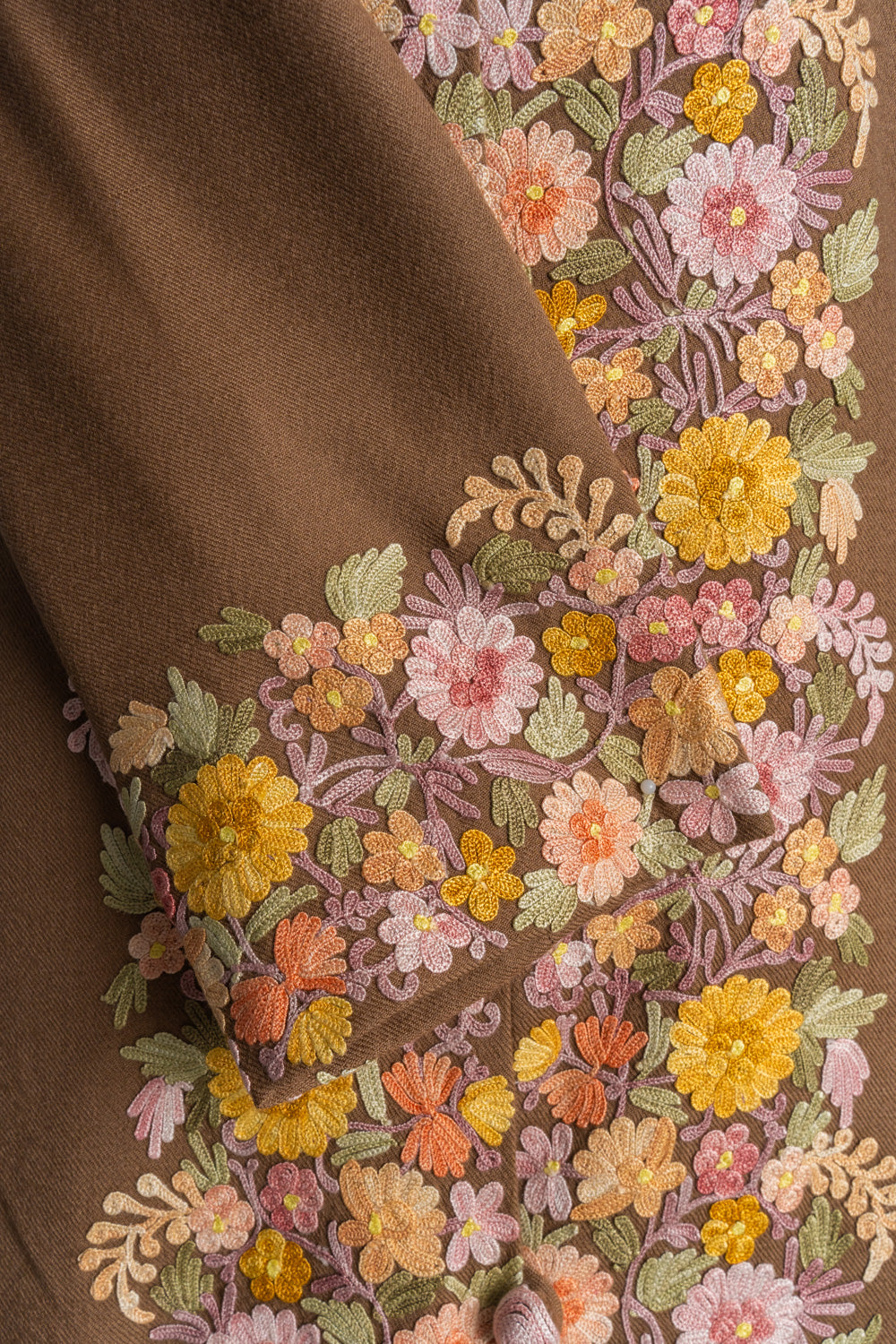 Close-up of the brown jacket’s folded cuff beside the front panel, both embroidered with pastel and yellow Aari flowers.
