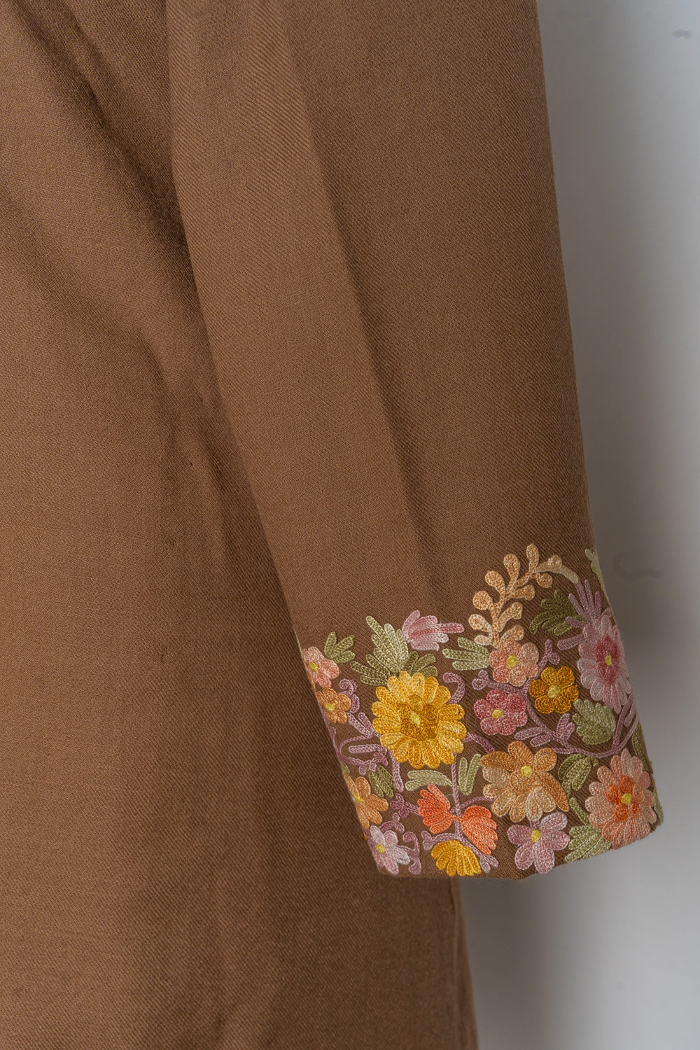 Brown jacket sleeve with a broad cuff of pink, peach and yellow flowers and green leaves.