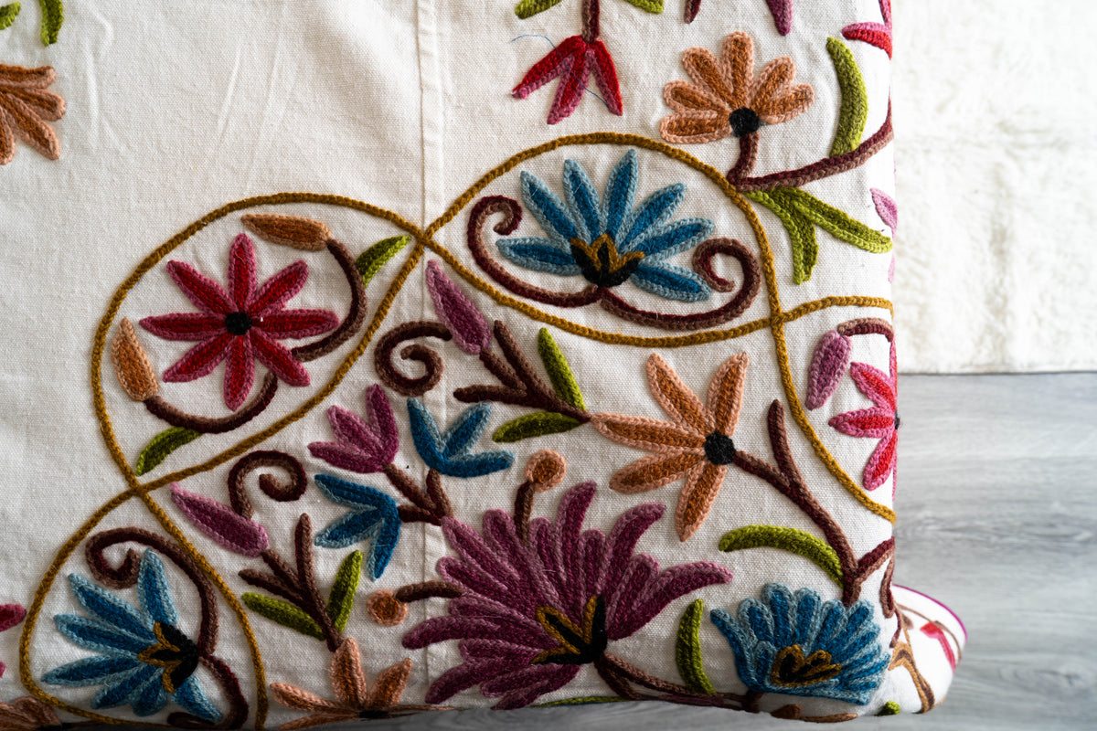 Close-up of raised crewel flowers in blue, burgundy, orange and green on a cream cushion.