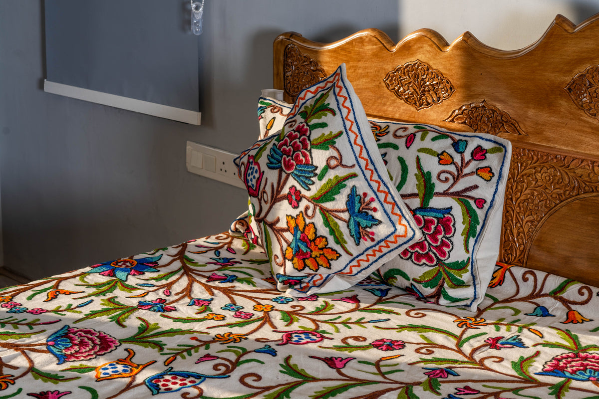 Matching embroidered cushion and pillow displayed against a carved wooden headboard above the cream floral bed cover.