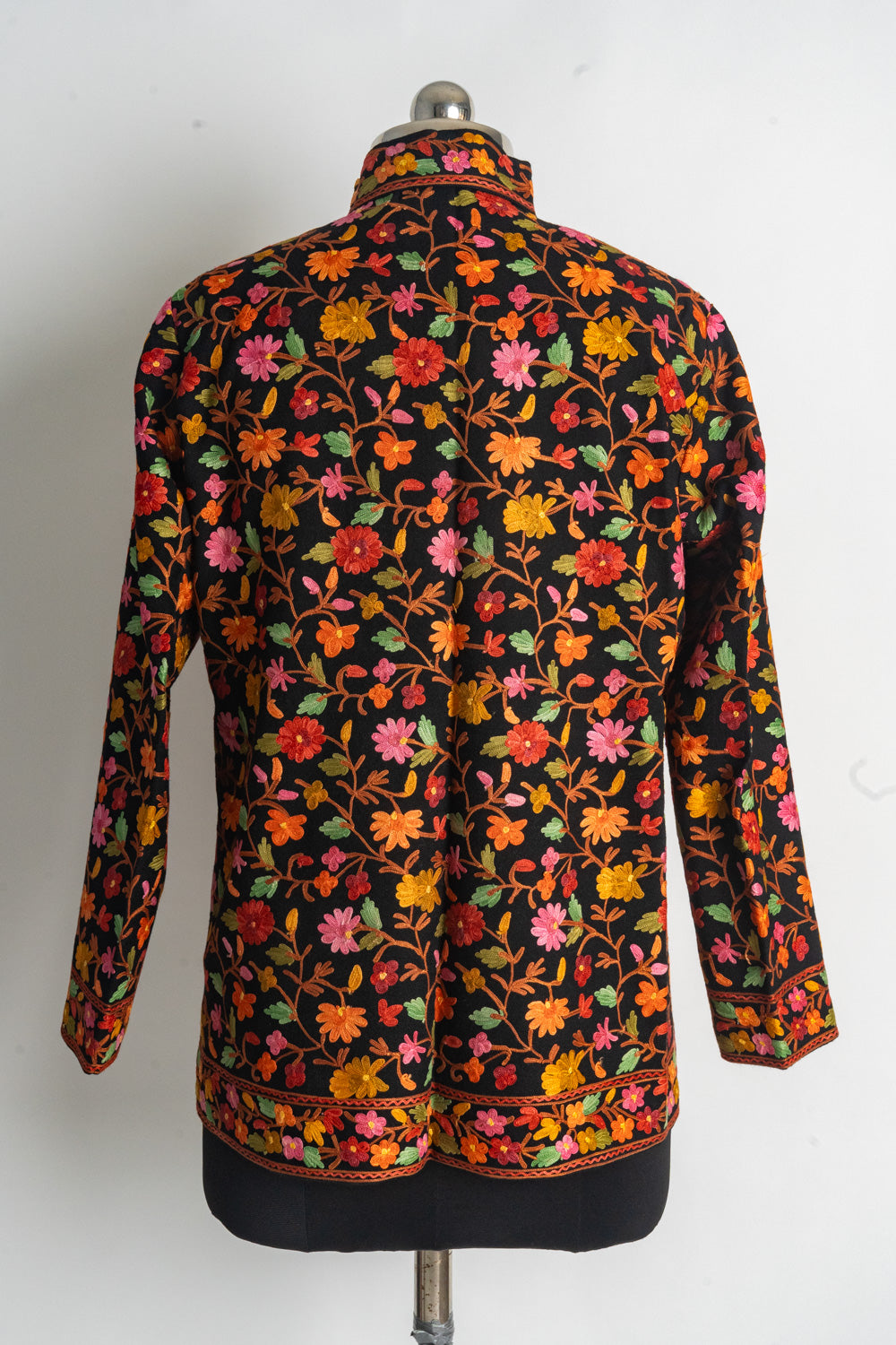 Back of a black short jacket covered in colourful Aari flowers and orange stems, with floral collar, cuffs and hem