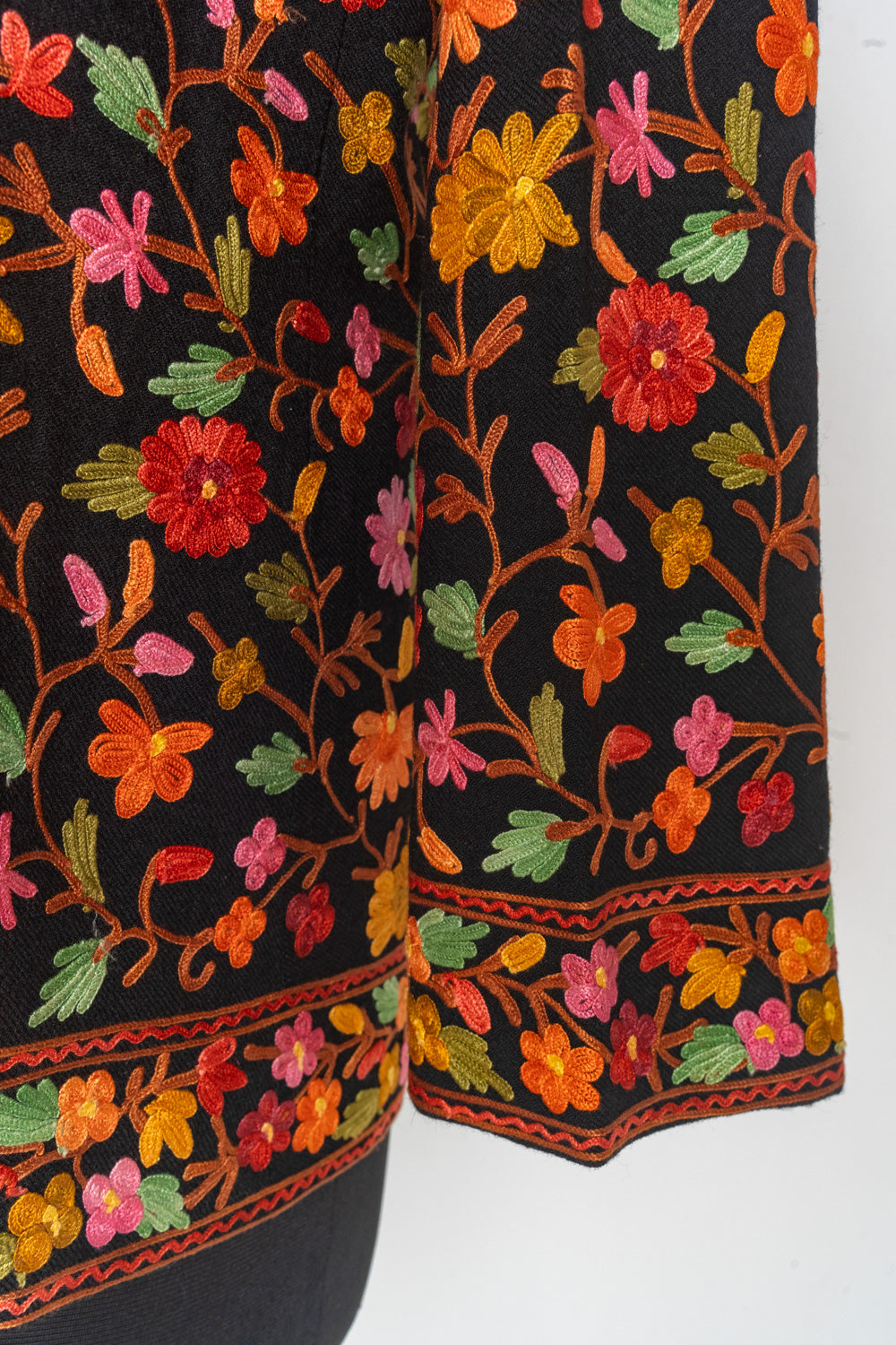 Black jacket cuff and hem with bright Aari floral bands below orange, pink and red flowers on branching stems