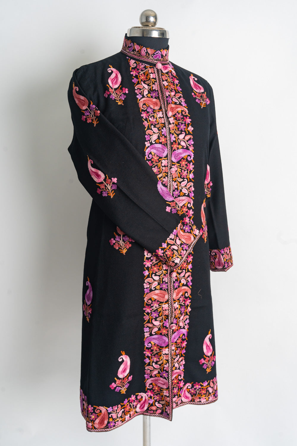 Angled full front of the black coat on a mannequin, with pink and purple embroidered borders and one sleeve crossed