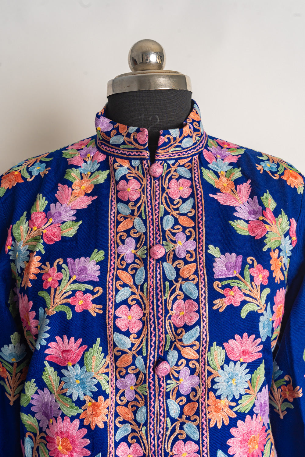 Upper front of the blue jacket with colourful flowers, a patterned stand collar and pink embroidered buttons.