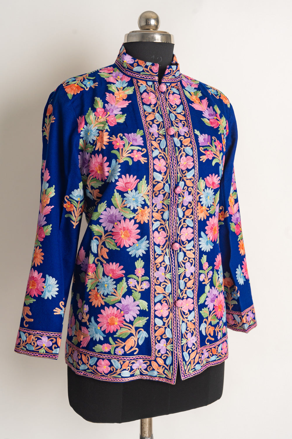 Angled front view of the deep-blue floral jacket showing its stand collar, embroidered buttons and patterned borders.