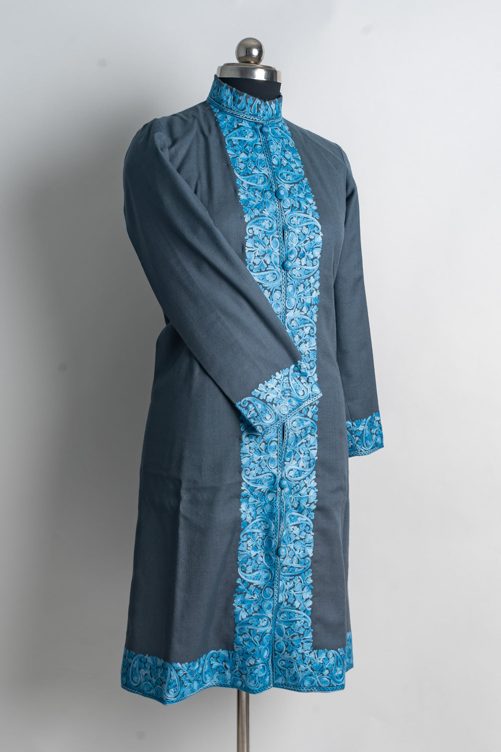 Angled full view of a grey jacket with bright blue embroidered borders at the collar, front, cuffs and hem.