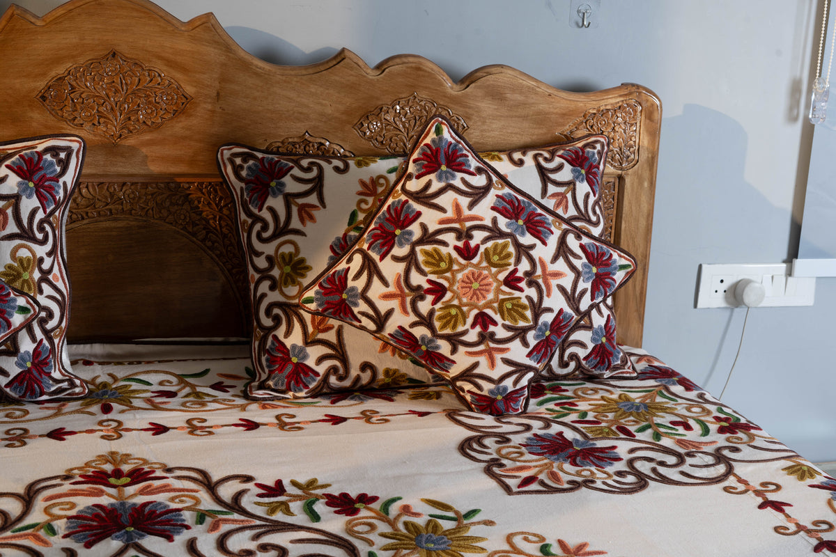 Matching cream Crewel pillow and cushion covers displayed on the floral bed cover, with brown vines and colourful flowers
