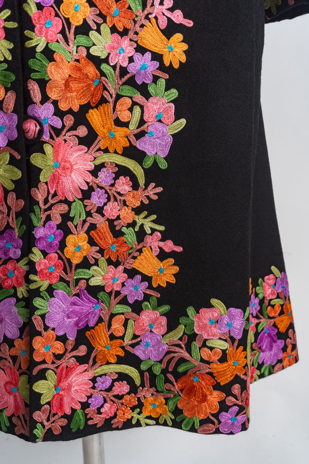 Detail of pink, orange and purple flowers with green stems bordering the black jacket’s lower front and hem.