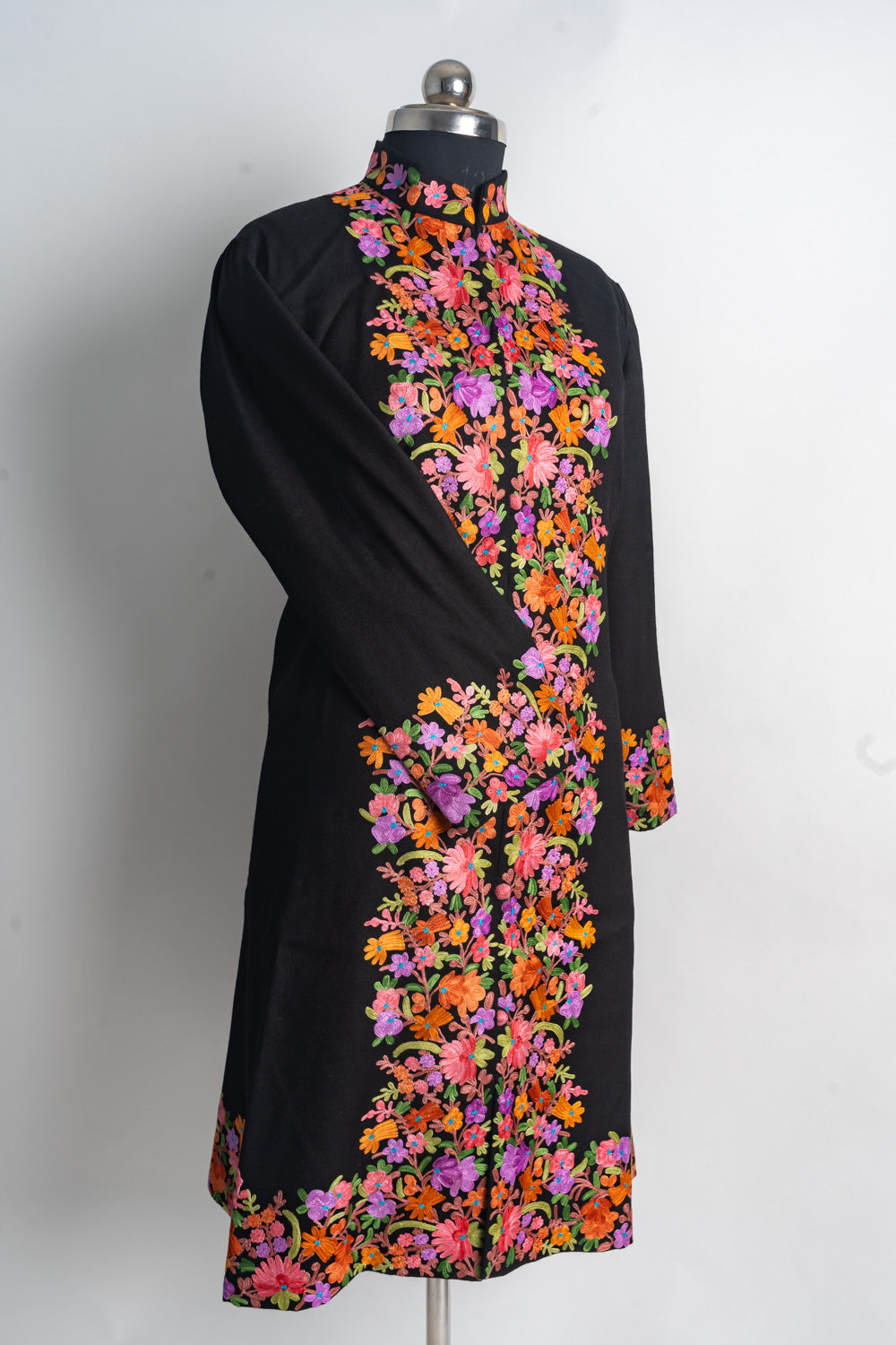 Full front of the black long jacket on a mannequin, with one sleeve crossed and bright floral borders from collar to hem.