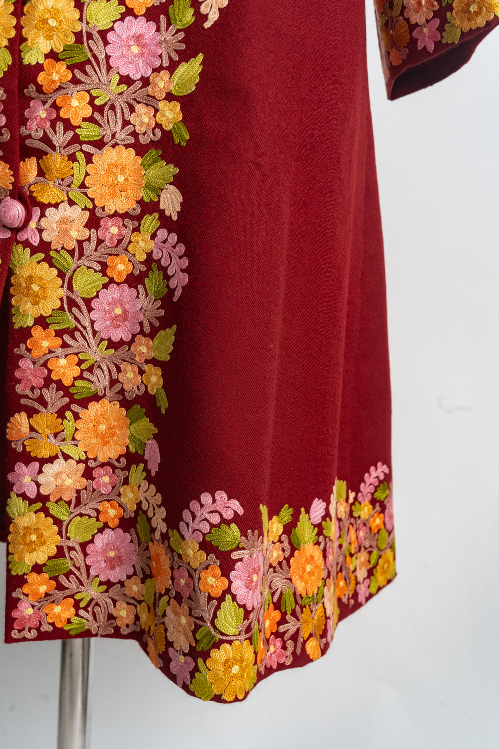 Lower corner of the ruby-red jacket with colourful Aari flowers and green leaves along the opening and hem