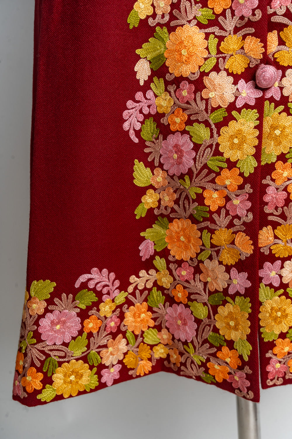 Detailed view of pink and orange flowers, yellow blossoms and green leaves around a covered button and the ruby jacket’s hem