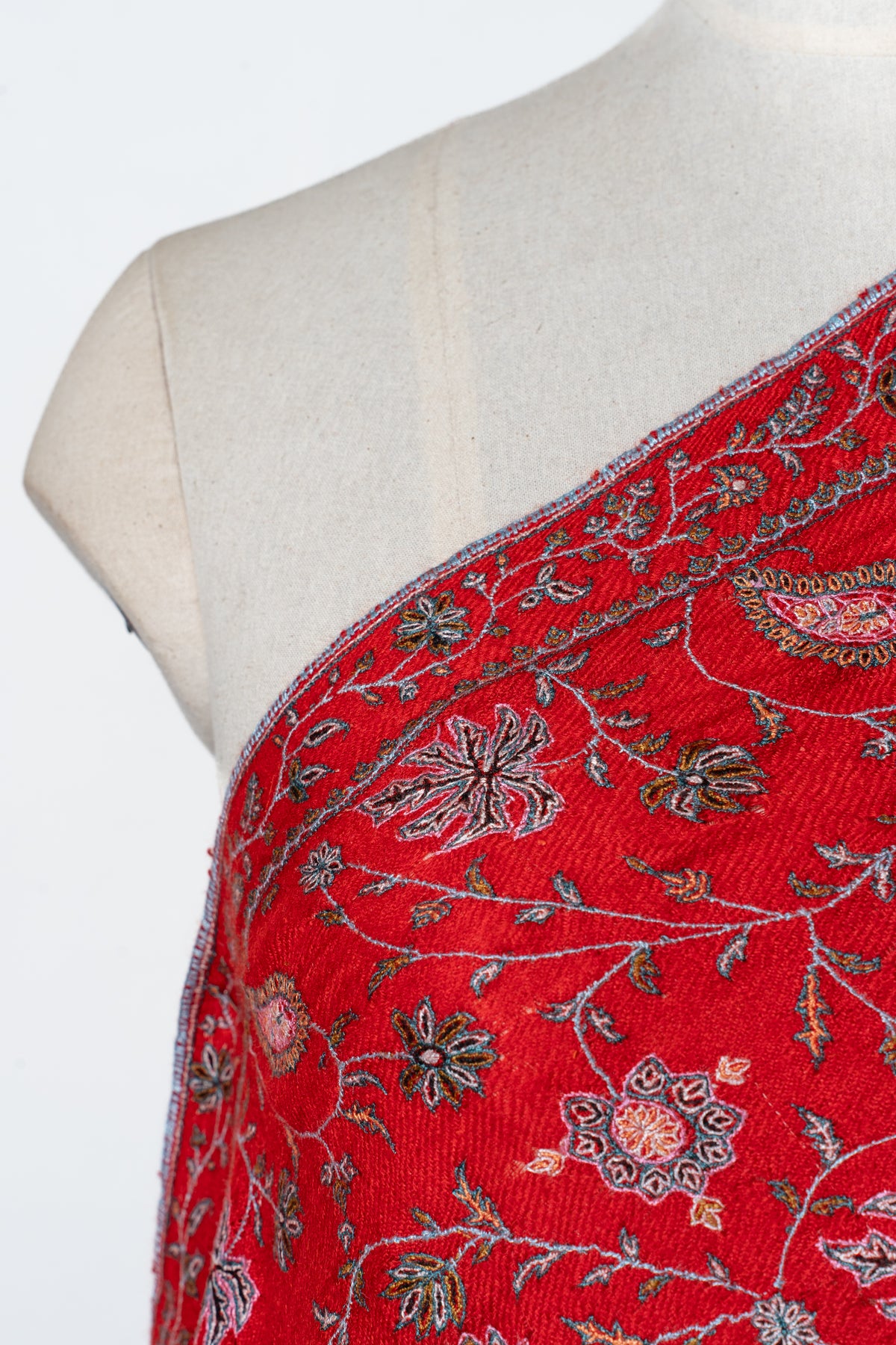 Shoulder detail of a scarlet shawl with pale Sozni flowers, lobed leaves and paisleys beside a narrow floral border