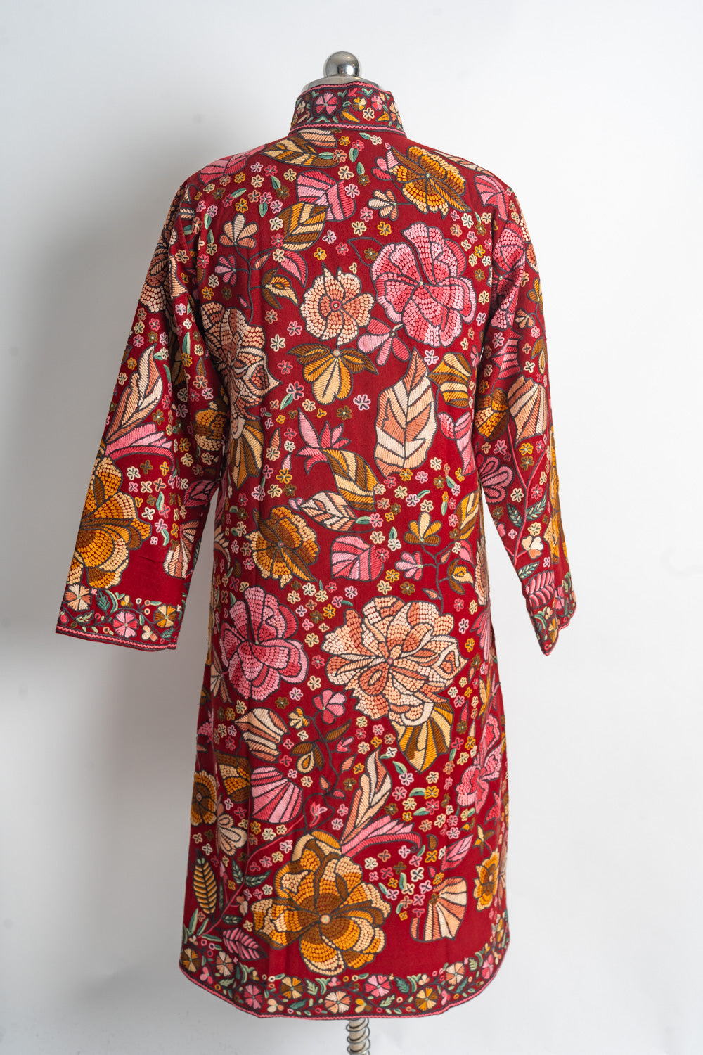Back of the red long jacket covered in large multicoloured flowers and leaves, with narrow floral borders at the cuffs and hem.
