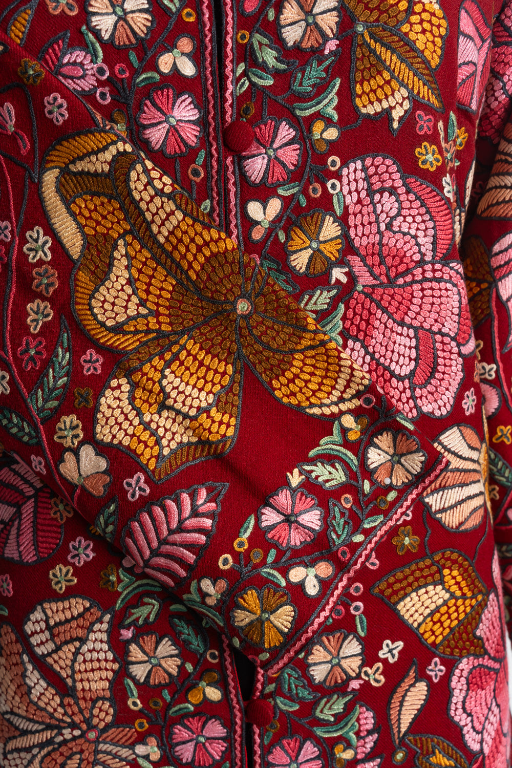 Close-up of a large orange flower and pink blossoms on the red jacket’s folded cuff beside the embroidered front opening.