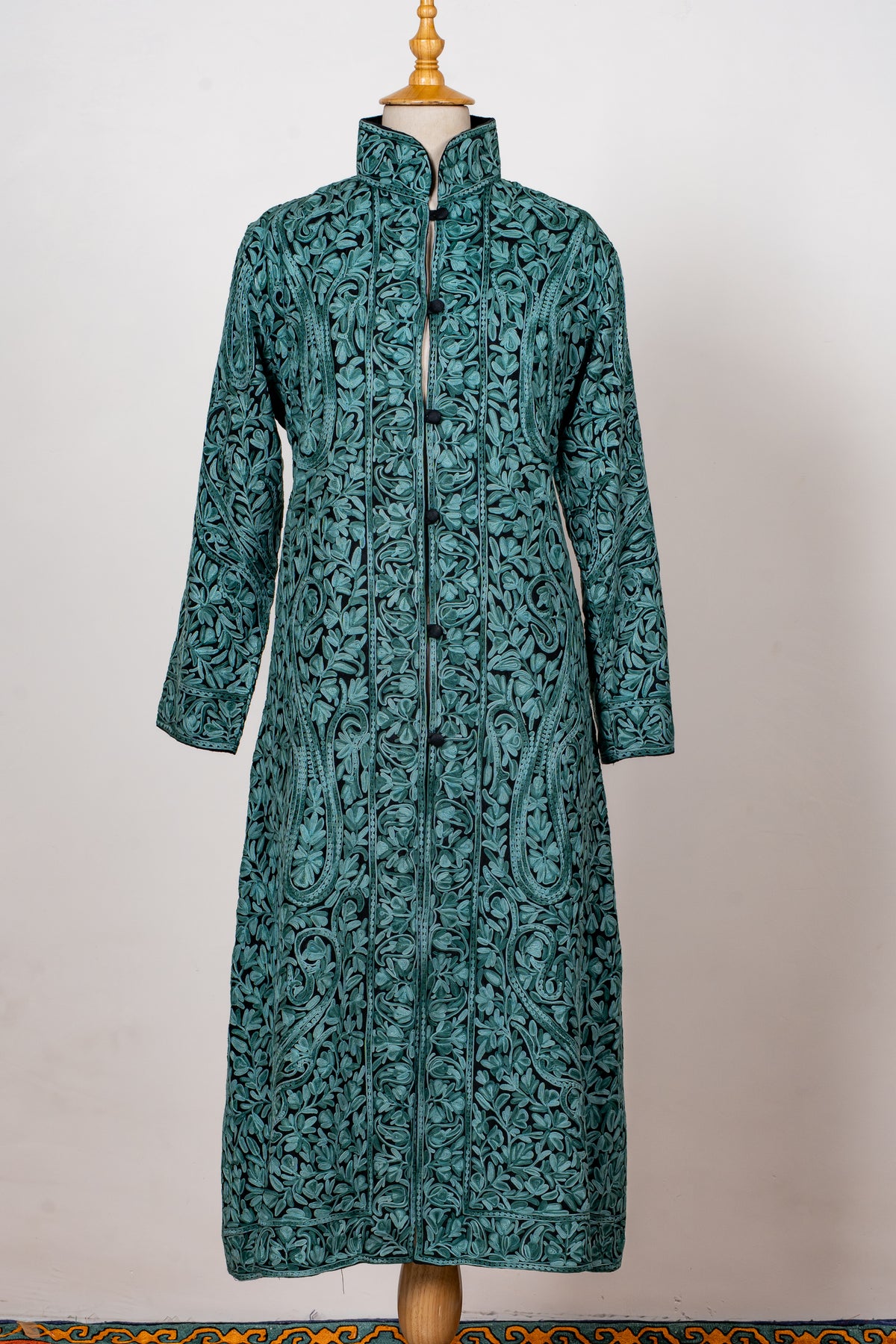 Full front of a teal long jacket with turquoise Aari floral vines, high collar and buttoned front, with both sleeves hanging