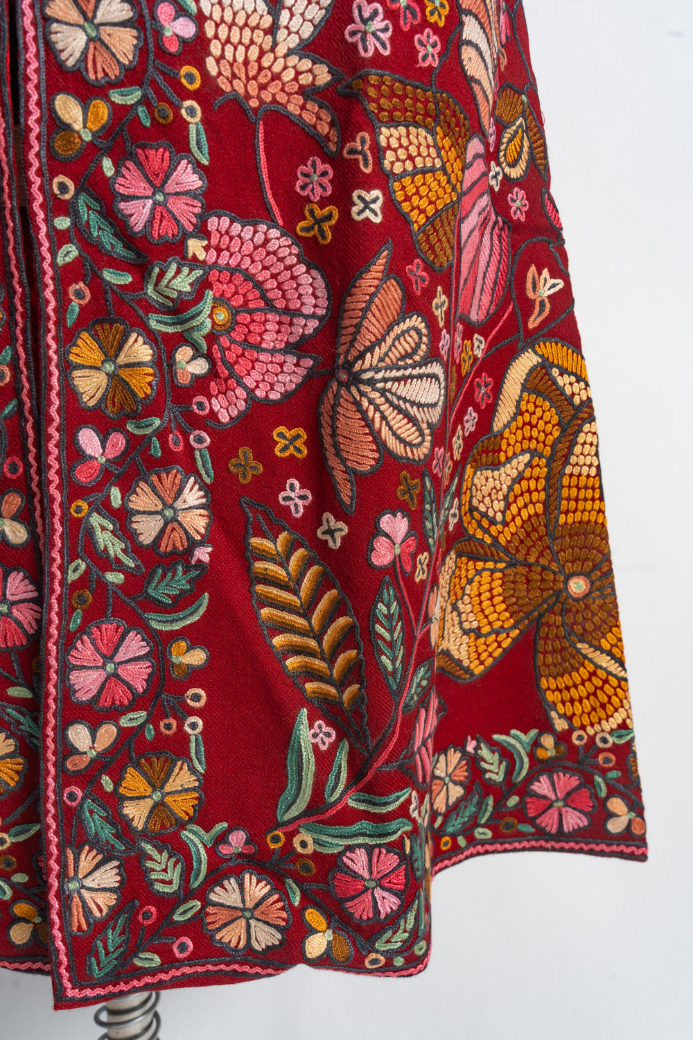 Detail of the red jacket’s lower front with large pink and orange flowers, green leaves and a narrow floral hem border.