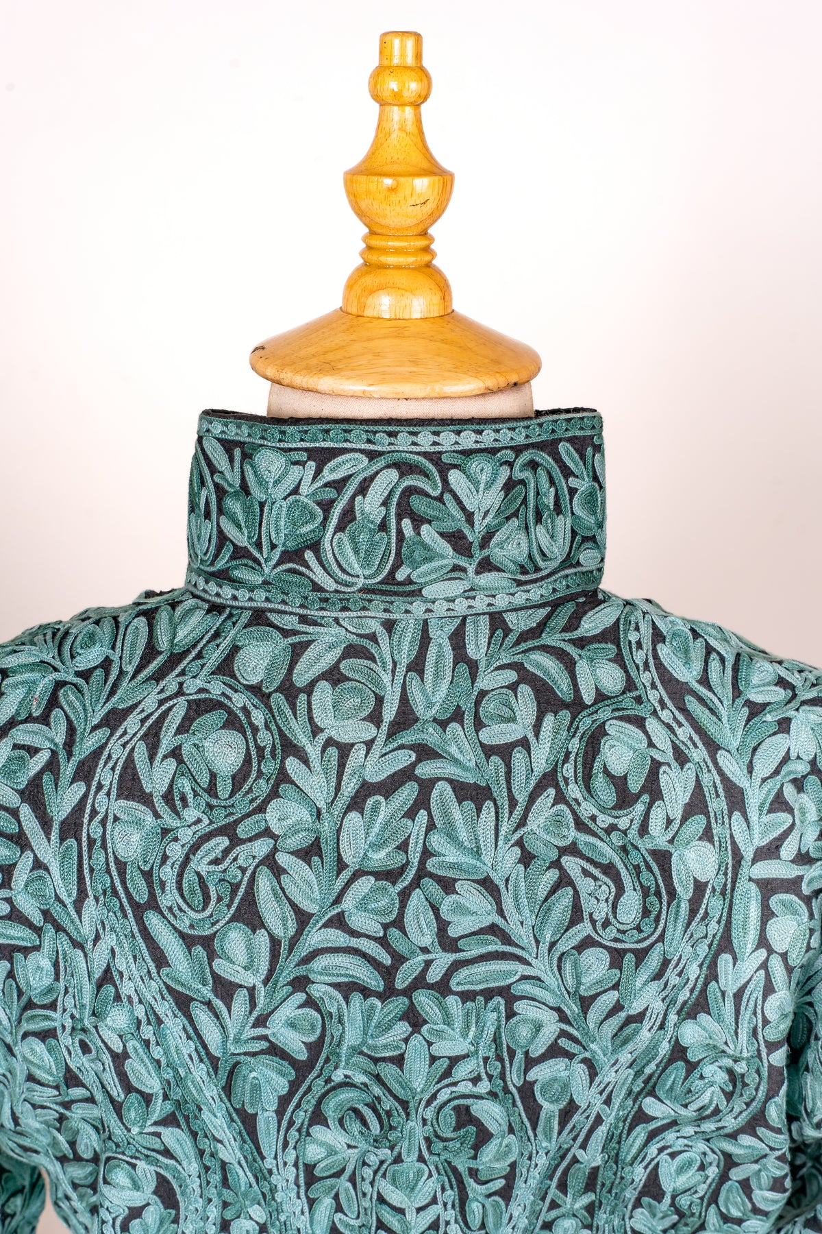 Close-up of a teal jacket's back collar and shoulders, showing dense turquoise Aari flowers, leaves and curling paisleys