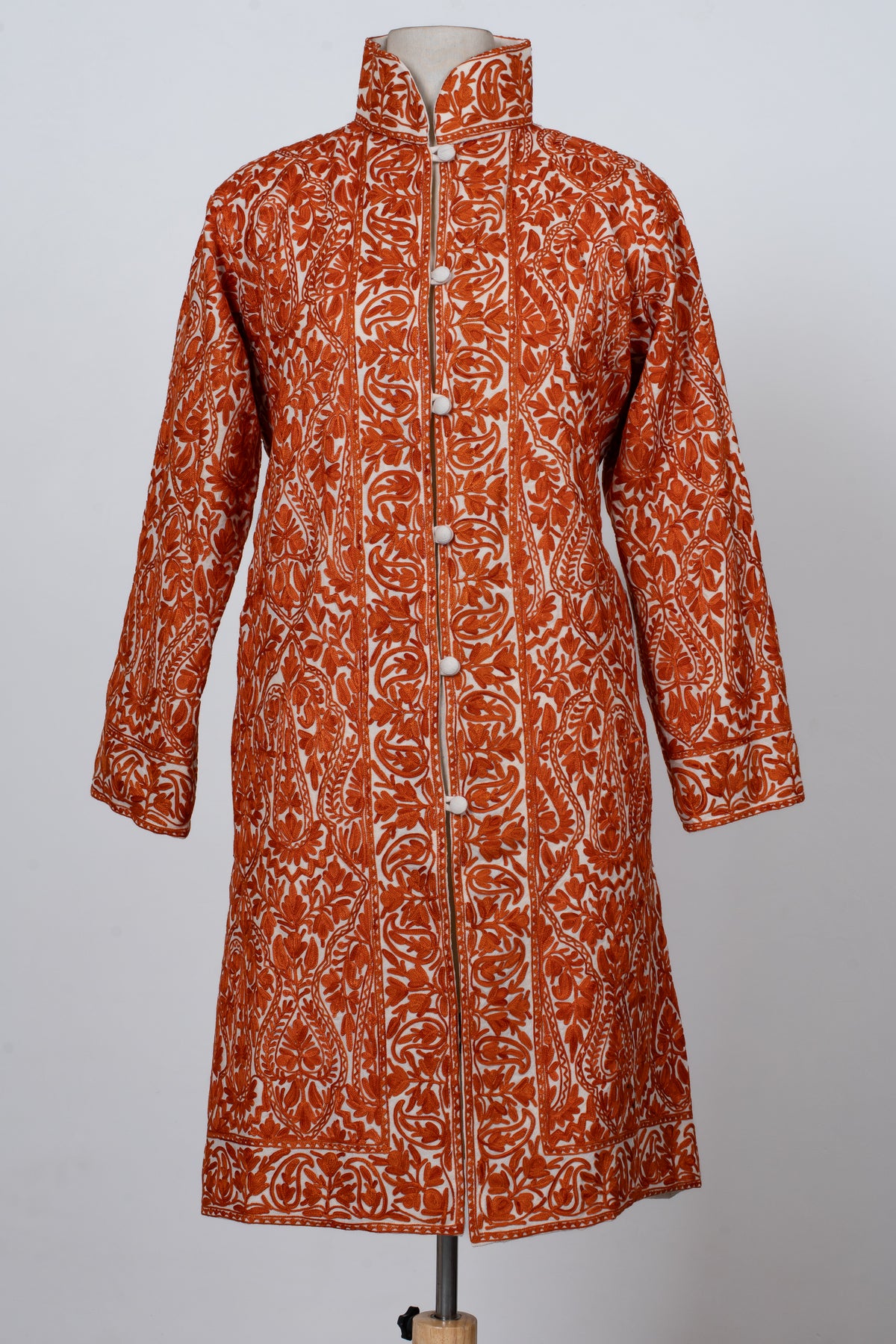 Full front view of the white jacket with orange Aari paisleys and leafy vines framed by broad patterned front bands.