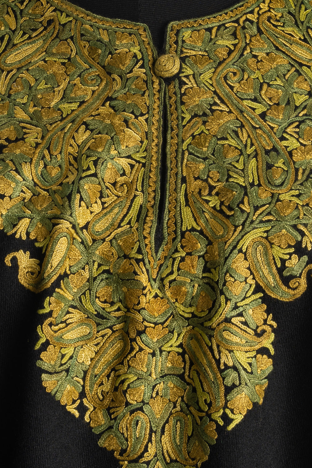 Close-up of golden yellow and olive green Aari paisleys and flowers around the buttoned slit neckline of a black poncho