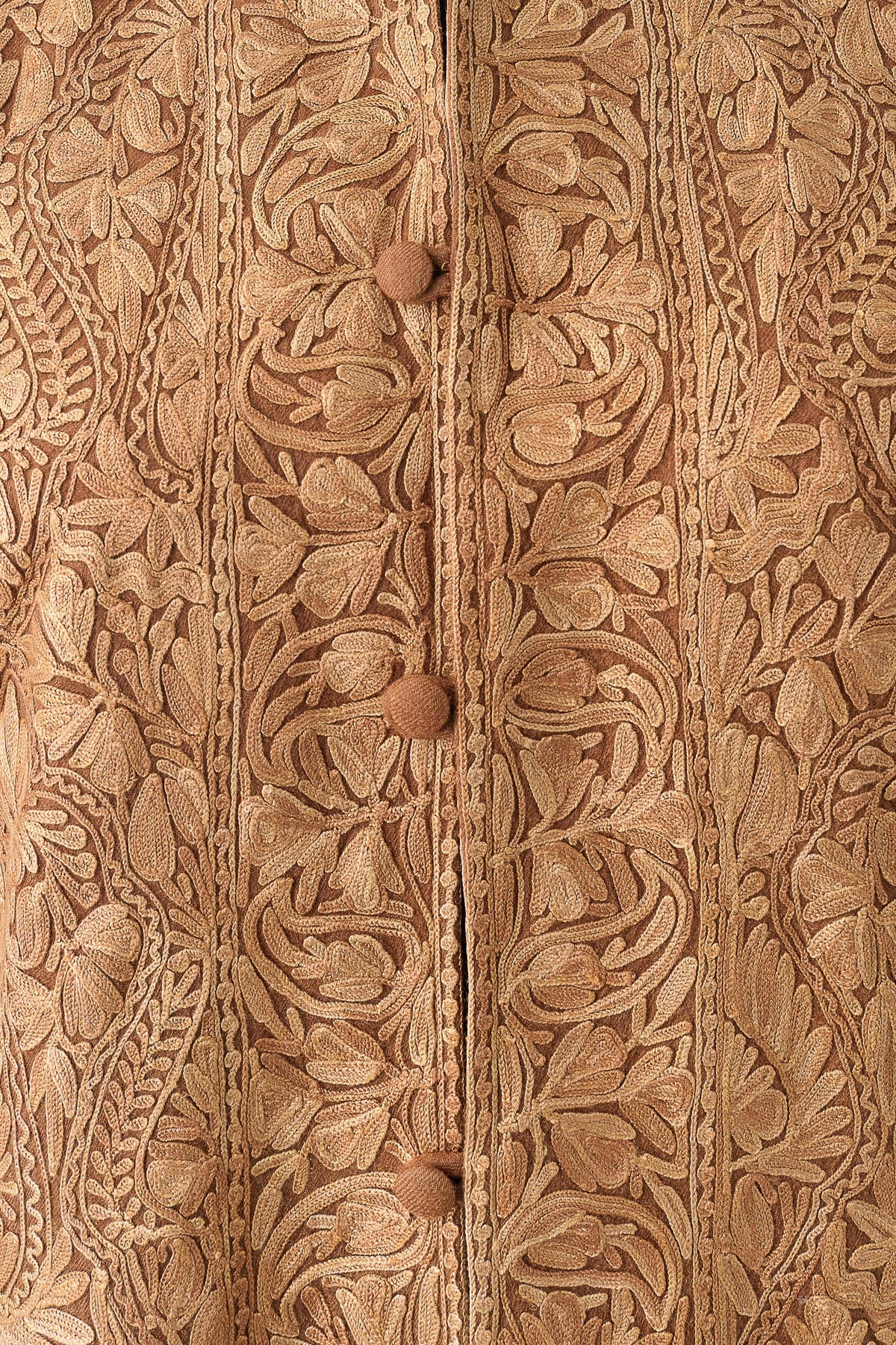 Close-up of tonal floral and paisley embroidery around the beige jacket's covered buttons