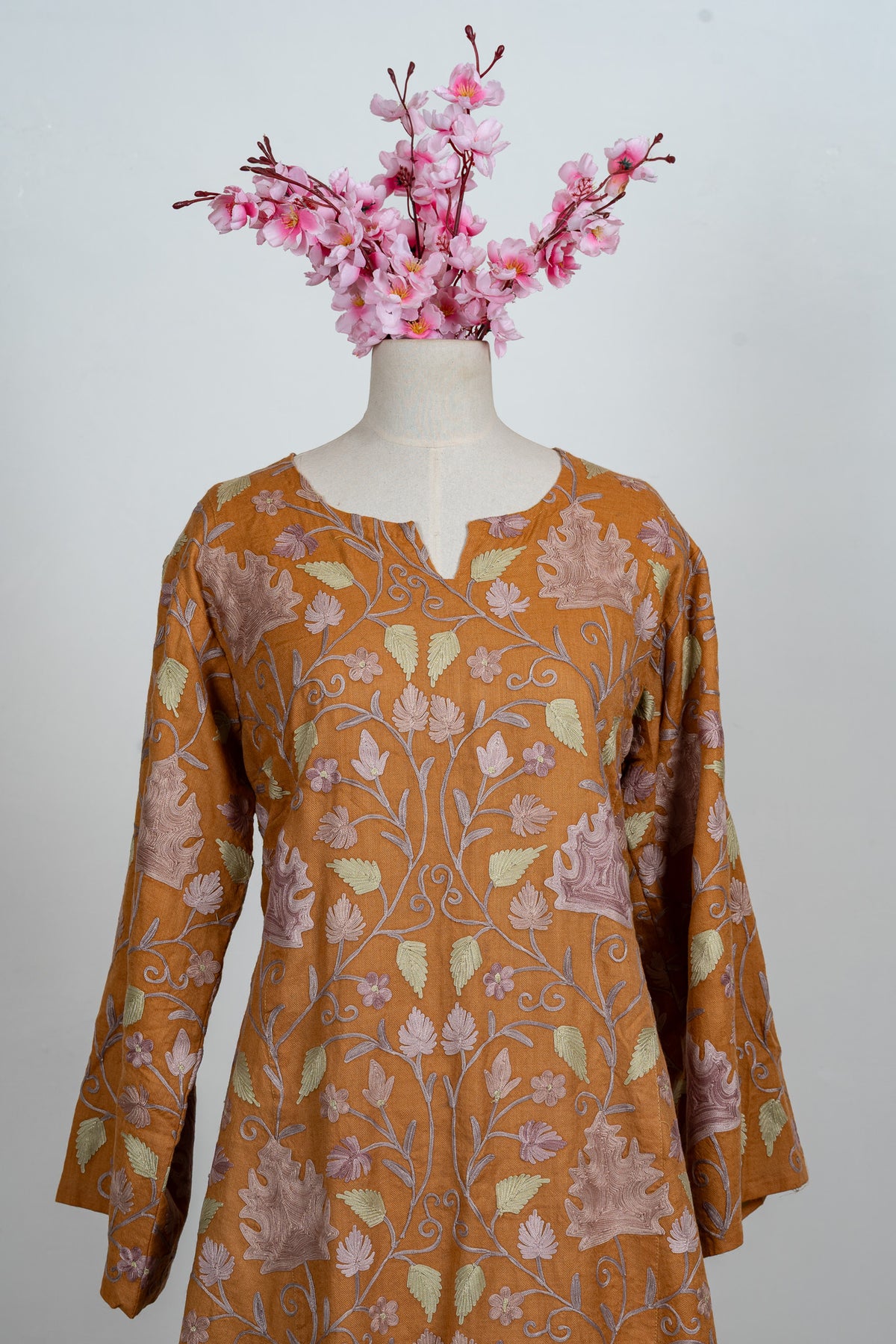 Front view of an amber abaya on a mannequin with a notched neckline and pale Aari leaves across the bodice and sleeves