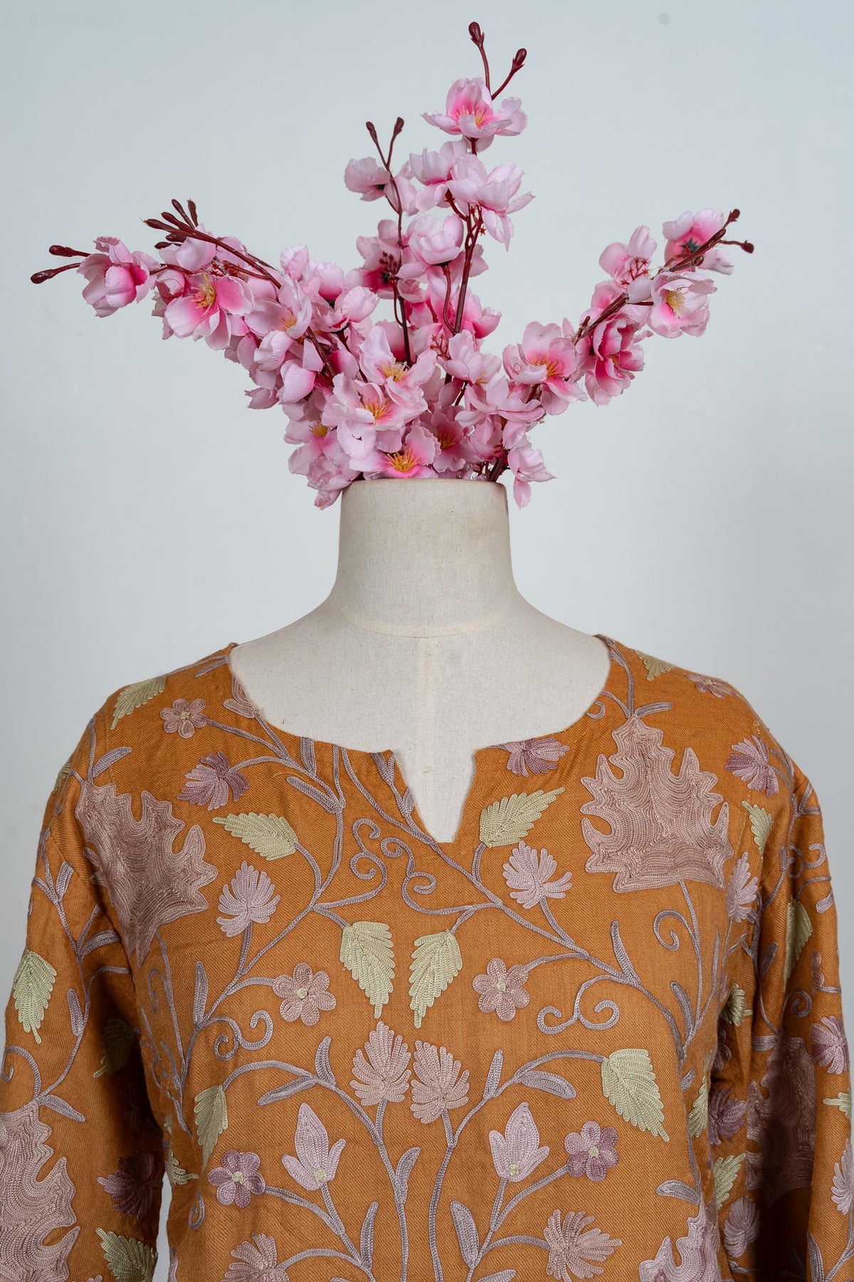 Upper front of an amber abaya with a notched round neckline and pale lilac and green Aari leaf embroidery