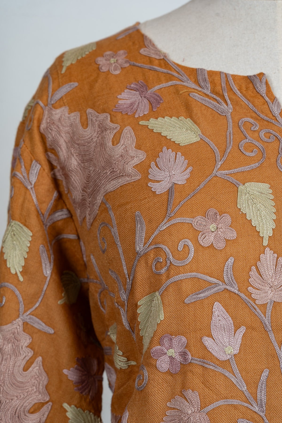 Close-up of an amber abaya's shoulder with large lilac Aari leaves, pale green leaves and fine curling stems