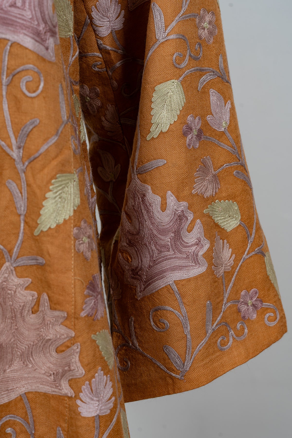 Detail of an amber abaya sleeve with lilac maple-shaped Aari leaves, pale green leaves and small flowers