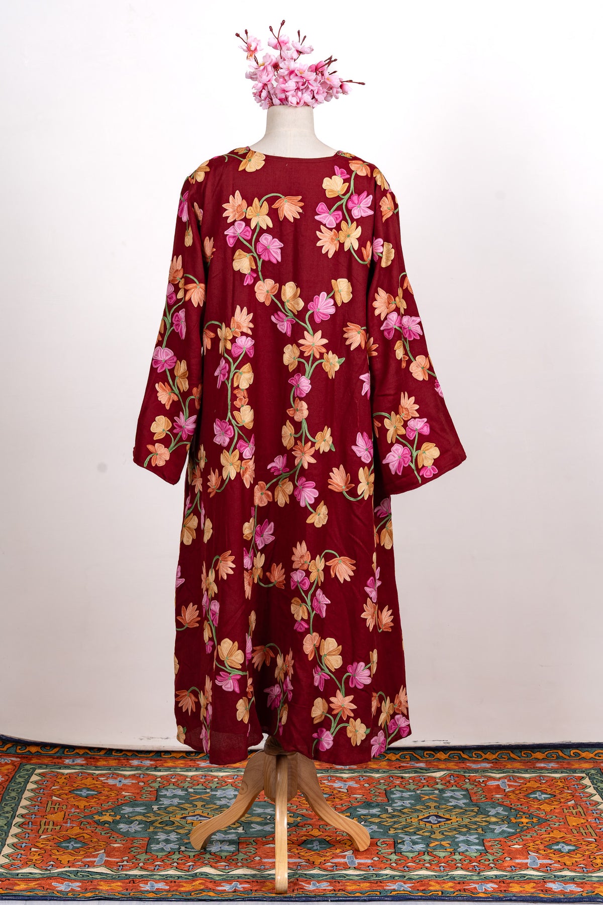 Full back view of the crimson abaya on a mannequin, showing its long silhouette and all-over multicoloured floral vines