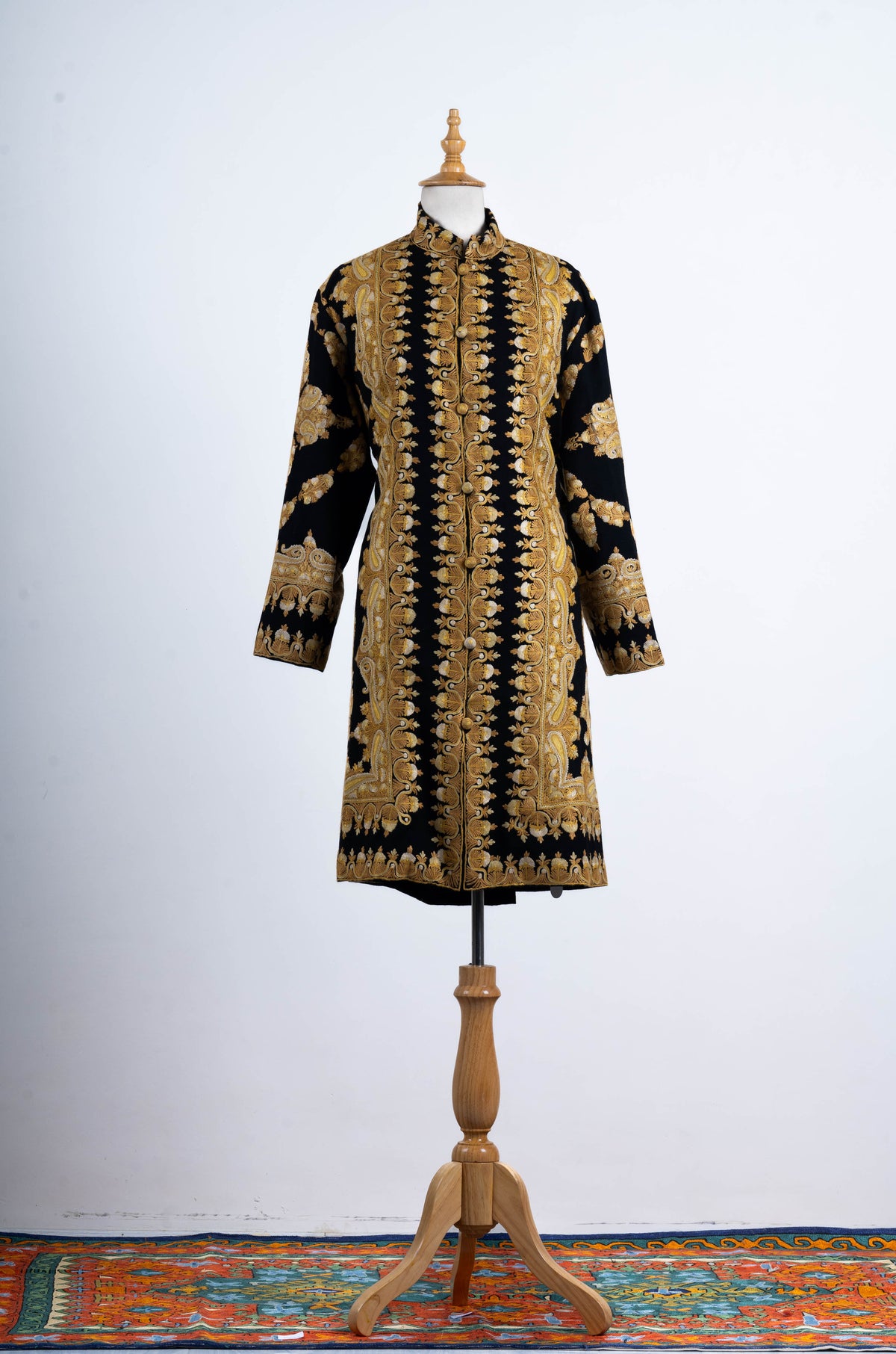 Straight-on full view of the black jacket with long gold-toned embroidered front borders, high collar and matching cuffs.