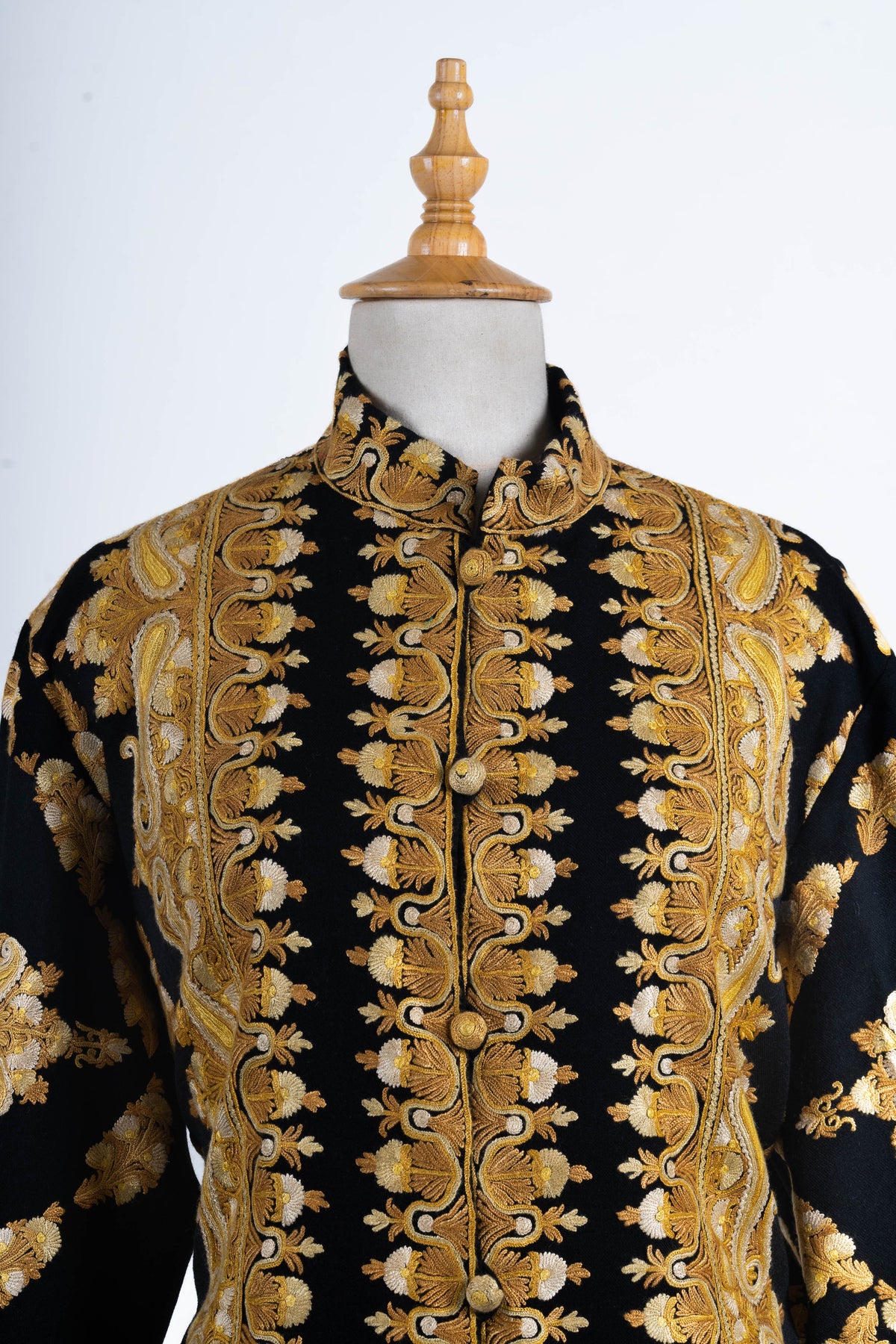 Upper front of the black jacket with a high embroidered collar, round covered buttons and dense gold-toned floral borders.