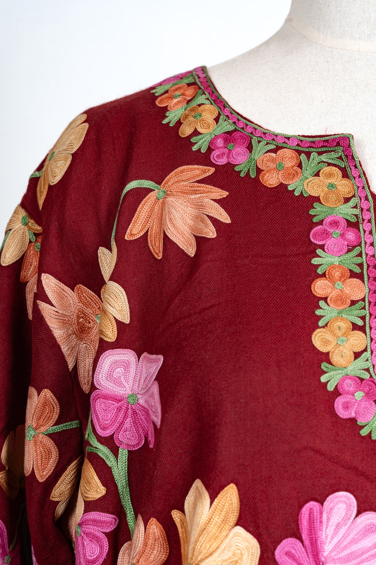 Detail of the crimson abaya’s shoulder and neckline, showing pink edging, small flowers and green embroidered leaves