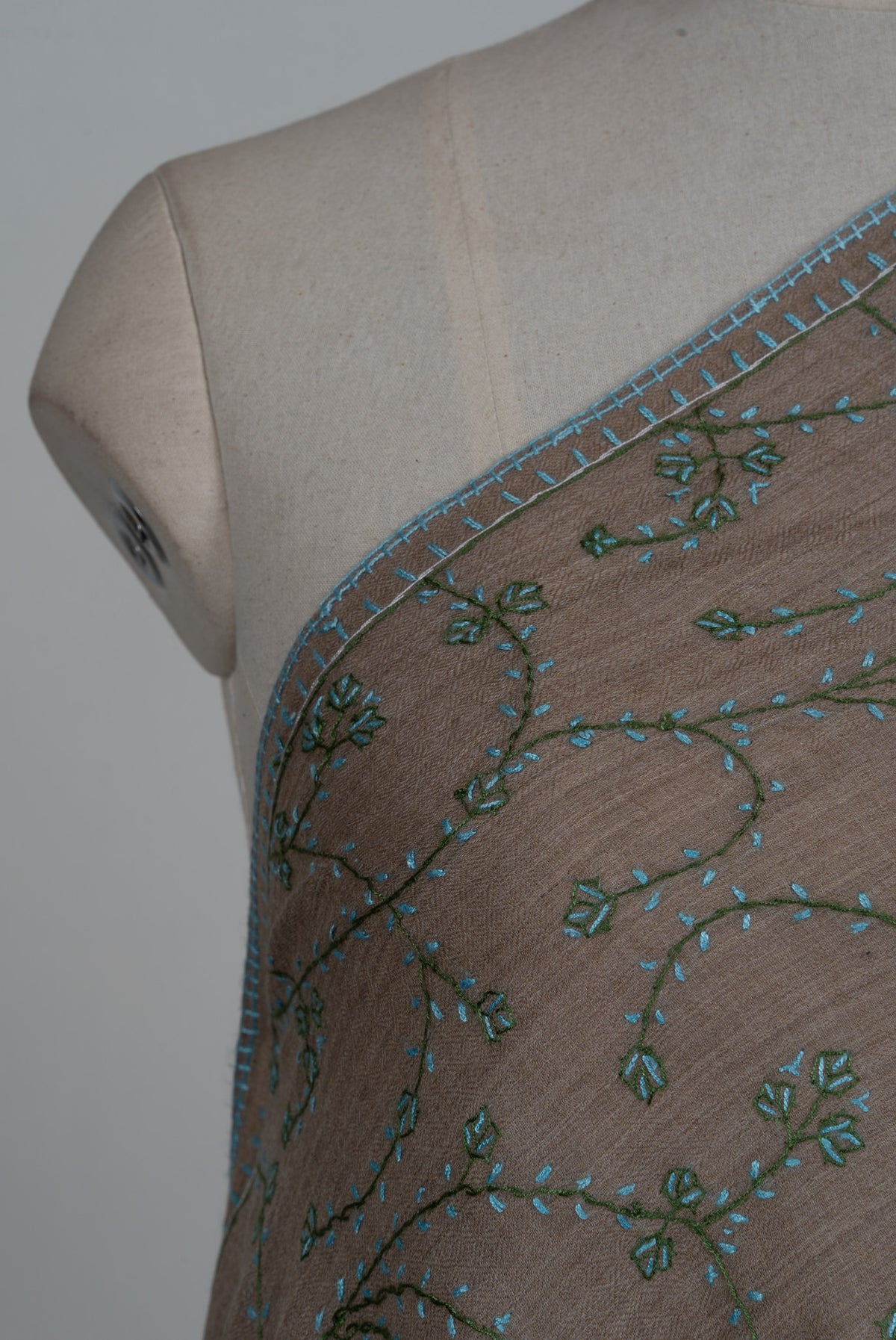 Shoulder detail of a taupe stole with dark teal Sozni stems, turquoise leaves and small green leaf clusters
