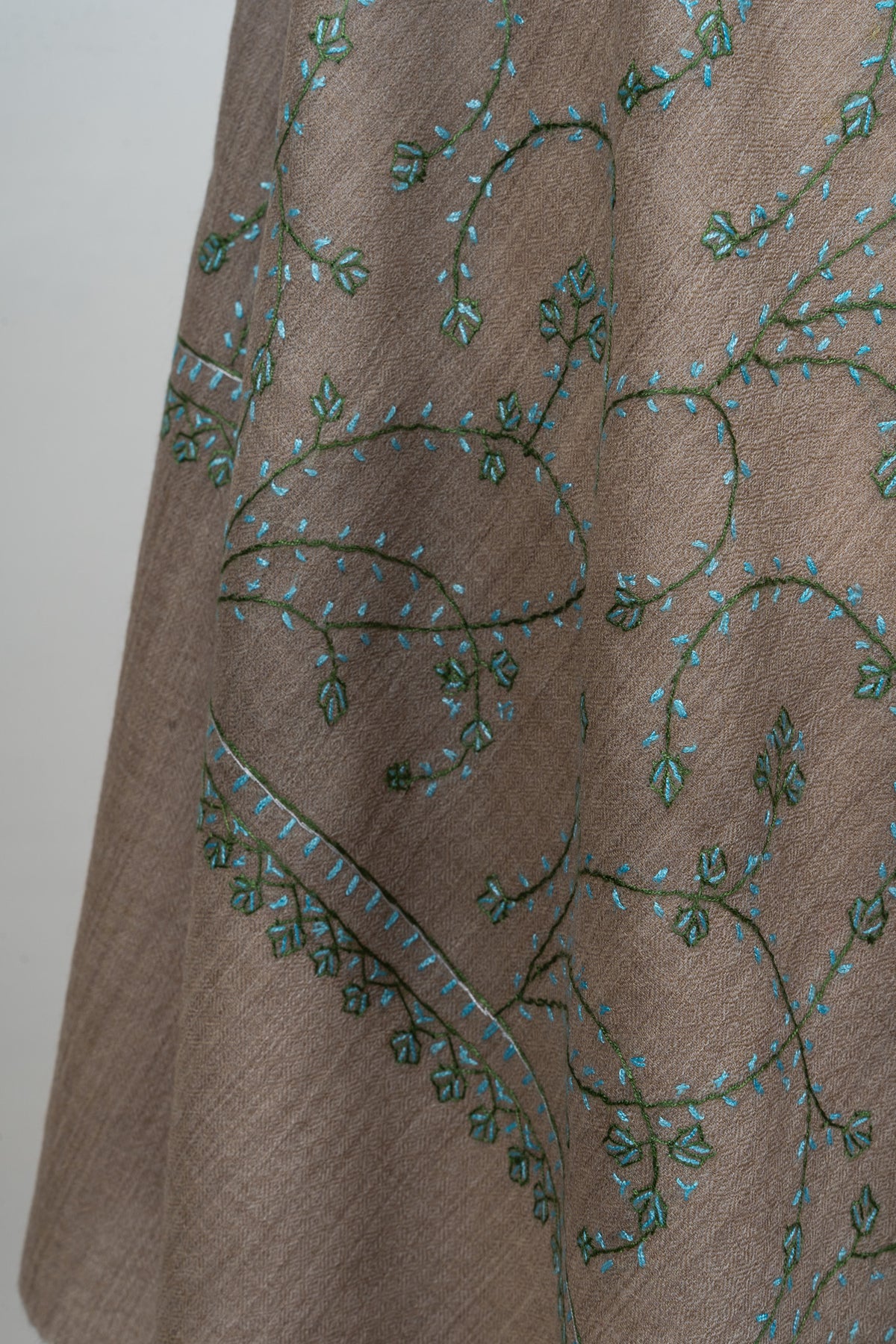 Hanging end of a taupe stole showing teal Sozni vines and small leaf clusters above a plain end band