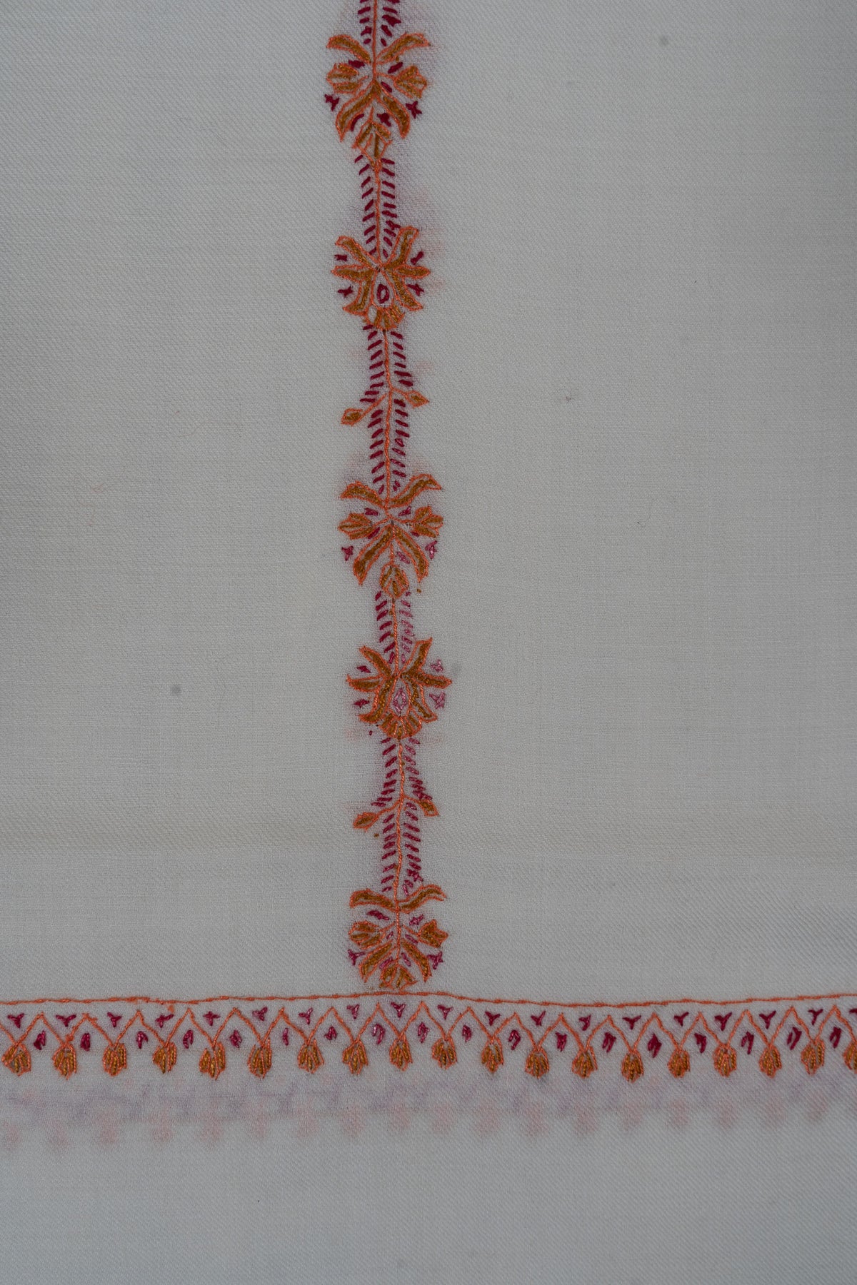 Close-up of orange Sozni flowers along a fine pink stem meeting the narrow embroidered end border on ivory fabric