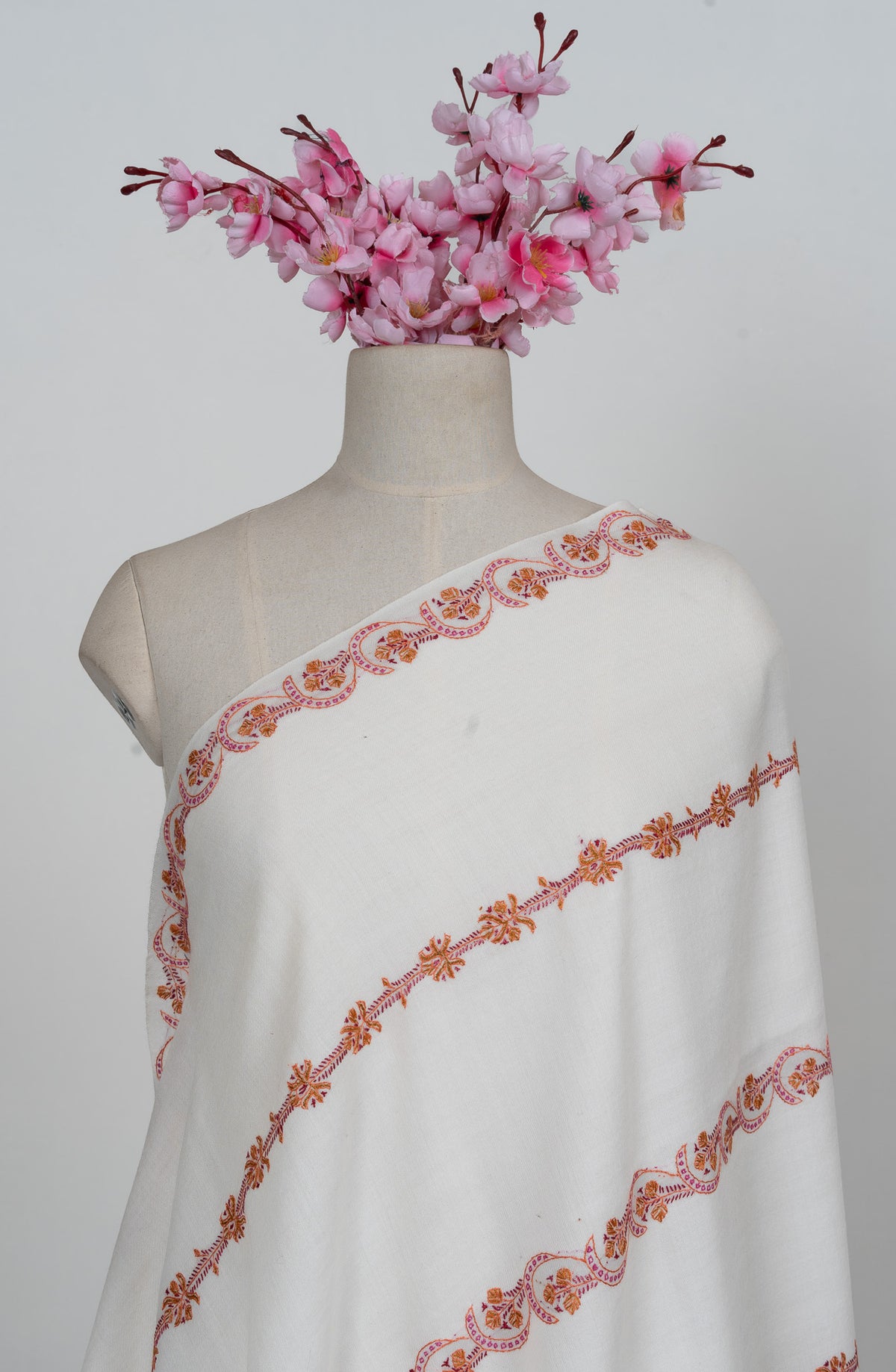 Upper view of an ivory shawl draped over one shoulder with spaced pink and orange Sozni floral bands