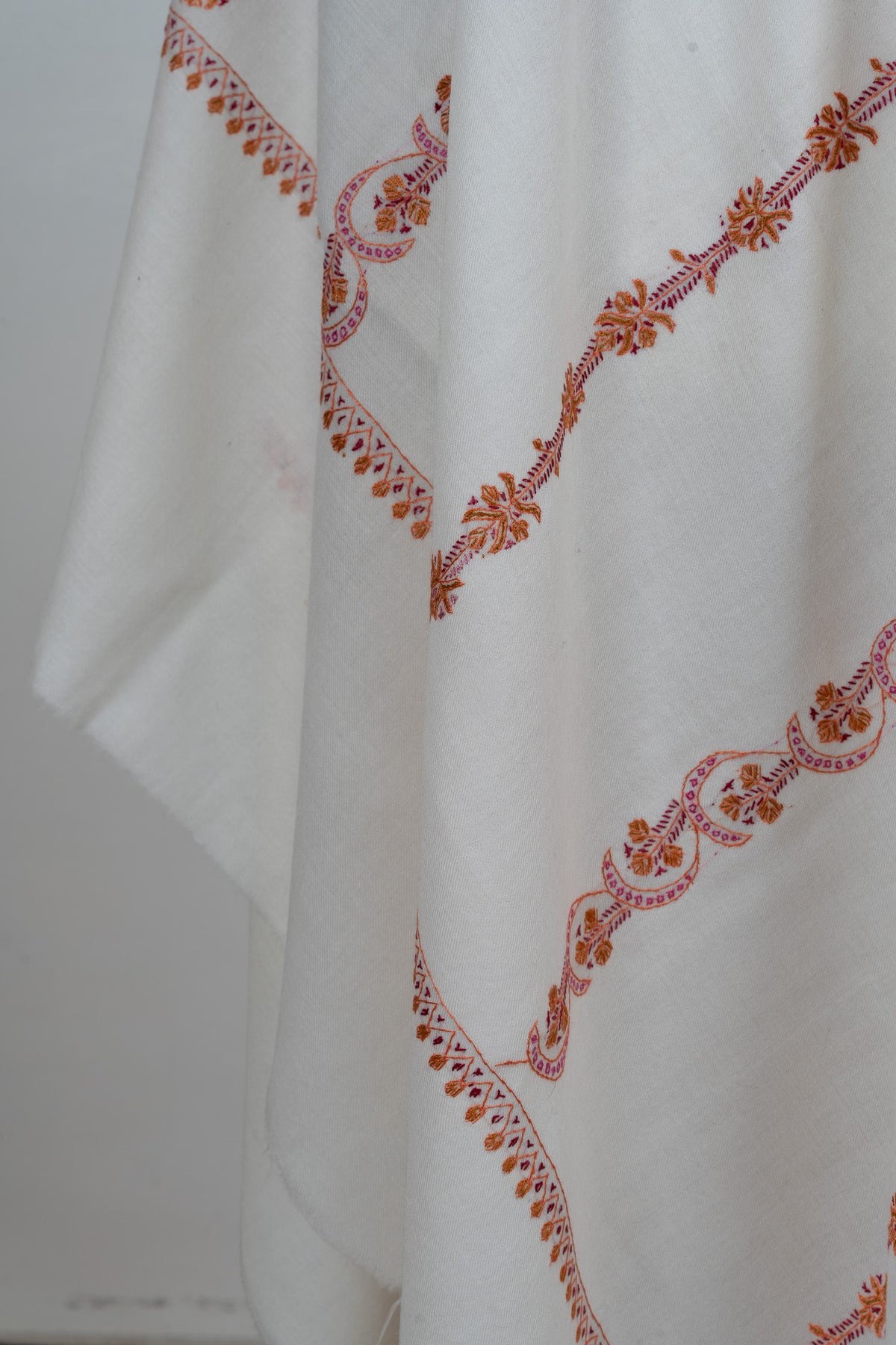 Folds of an ivory shawl with spaced pink and orange Sozni stripes and small leaf motifs along the end border