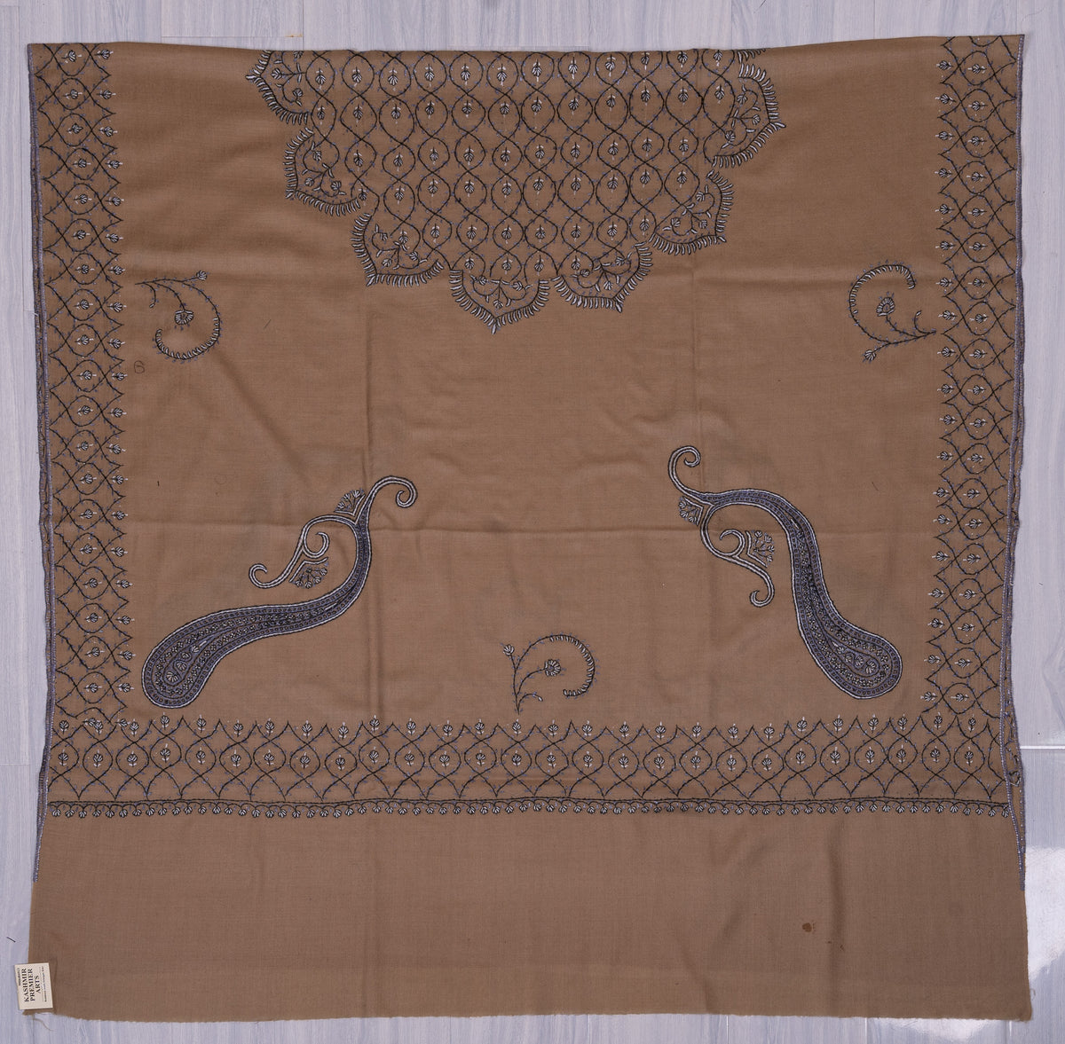 Desert-beige Merino wool shawl laid flat, with blue-grey paisleys, curling flower stems and a scalloped lattice panel