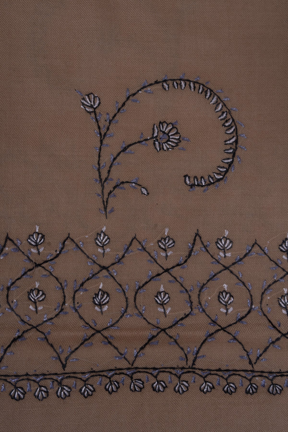 Close-up of a curling Sozni flower stem above a blue-grey lattice border on desert-beige fabric