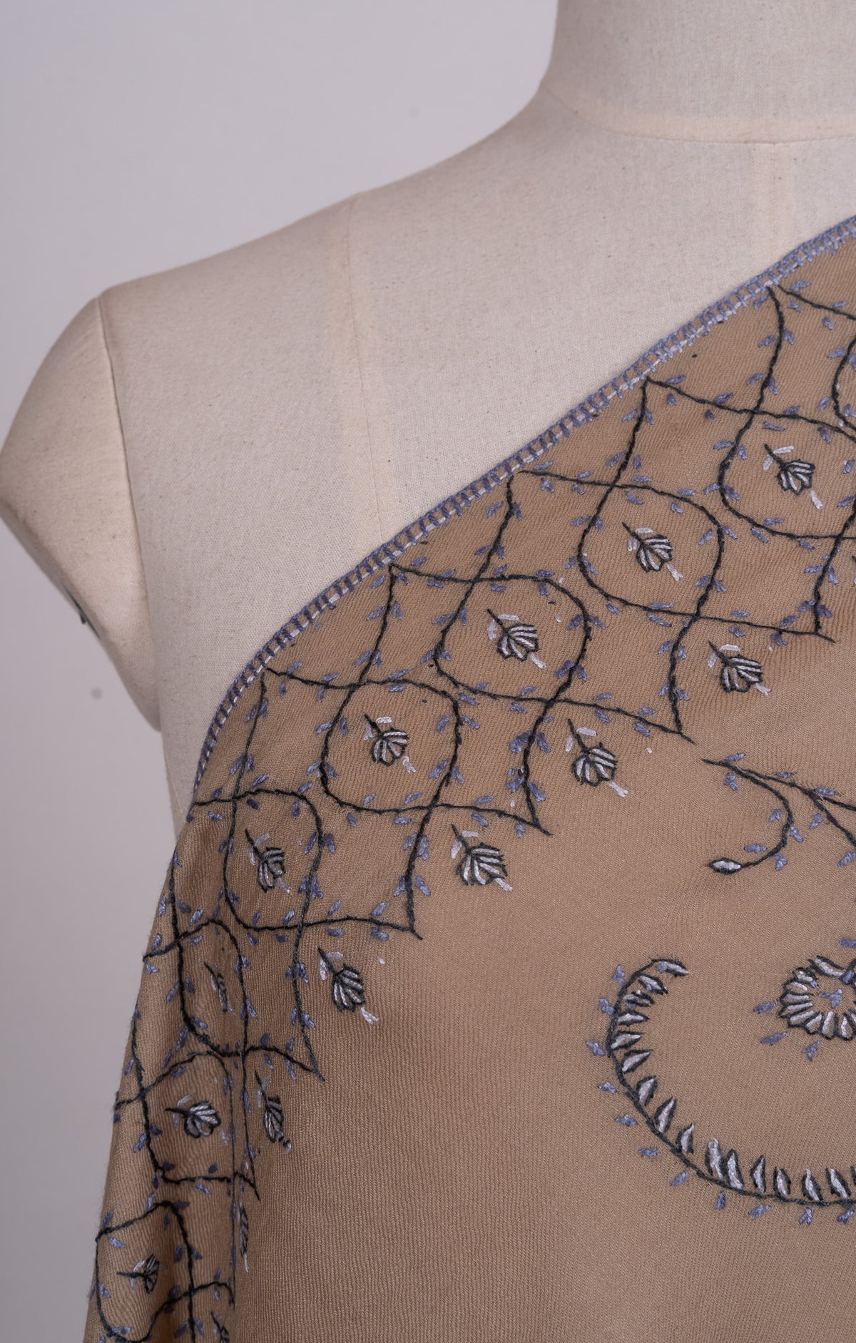 Close-up of a blue-grey Sozni lattice border and curling floral motif across a desert-beige shawl's shoulder